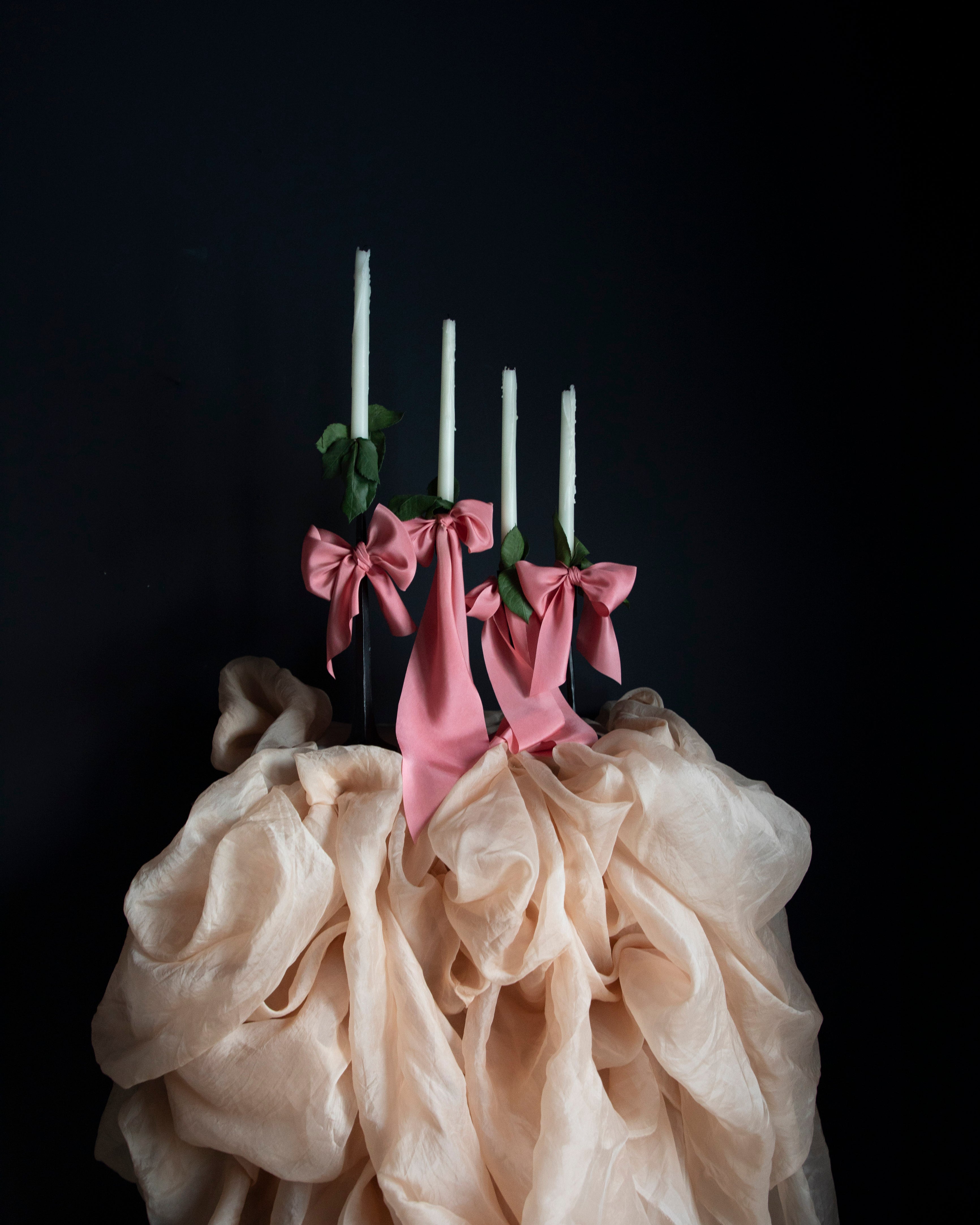 Decorative setup with pink ribbons, candles, and beige fabric against a black background