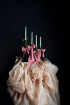 Decorative setup with pink ribbons, candles, and beige fabric against a black background