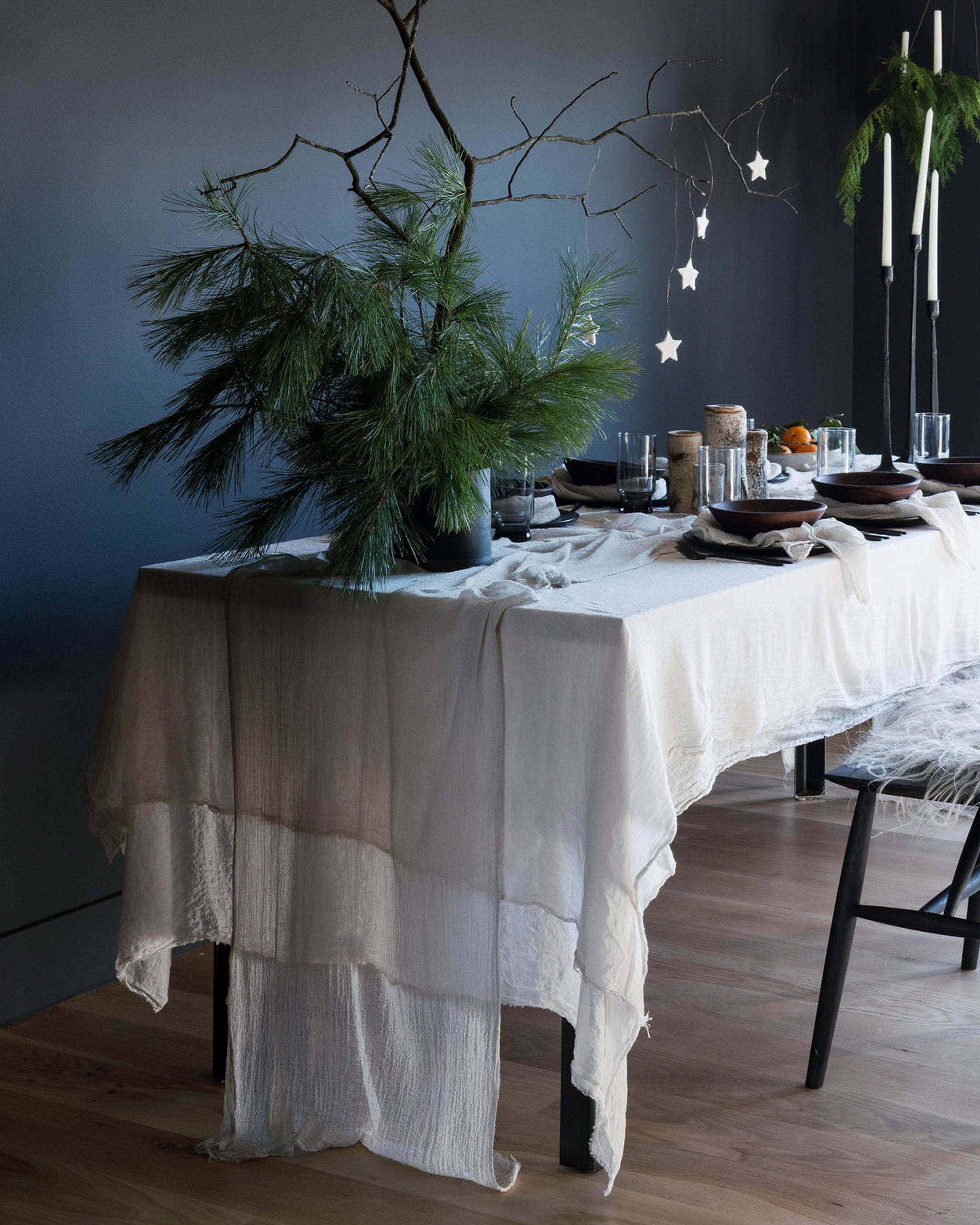 An elegantly set Nordic winter table featuring antique white, plant-dyed, handloomed cotton table runner, showcasing a wabi-sabi, organic design that highlights the heirloom quality of the table linens. Perfect for anyone seeking to create a serene and sophisticated winter tablescape.