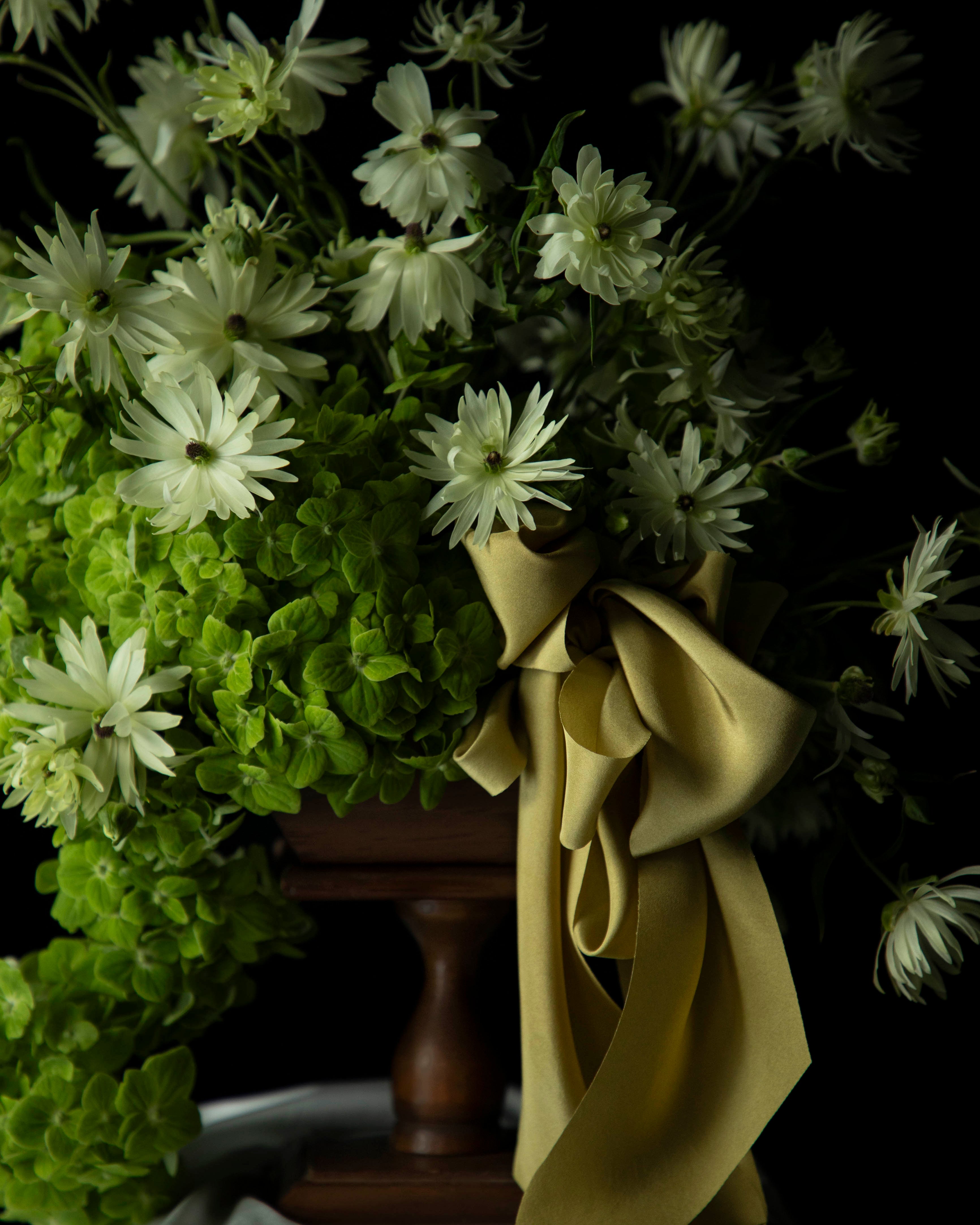 Floral arrangement with greenery and a citrus yellow ribbon on a dark background