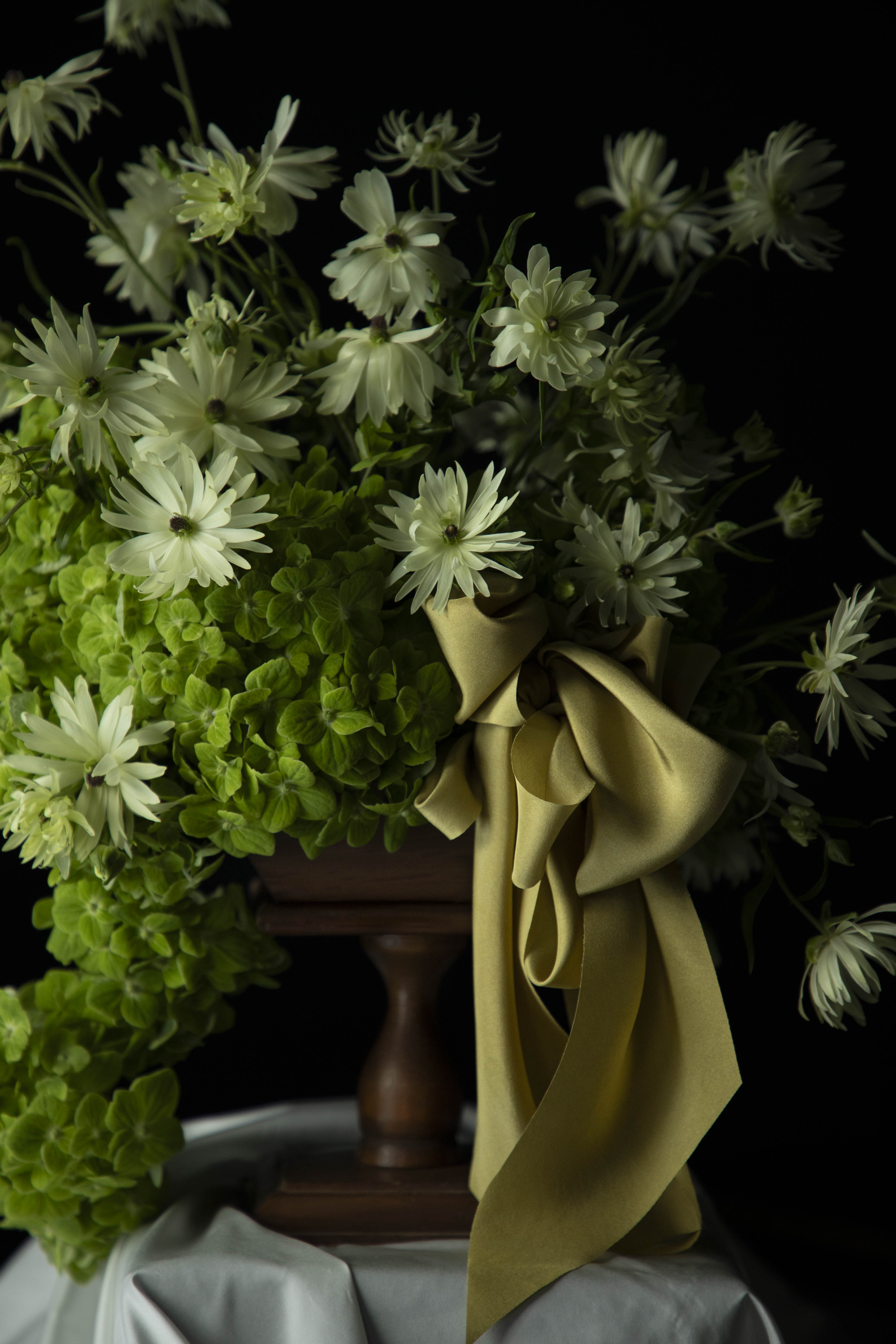 Floral arrangement with greenery and a citrus yellow ribbon on a dark background