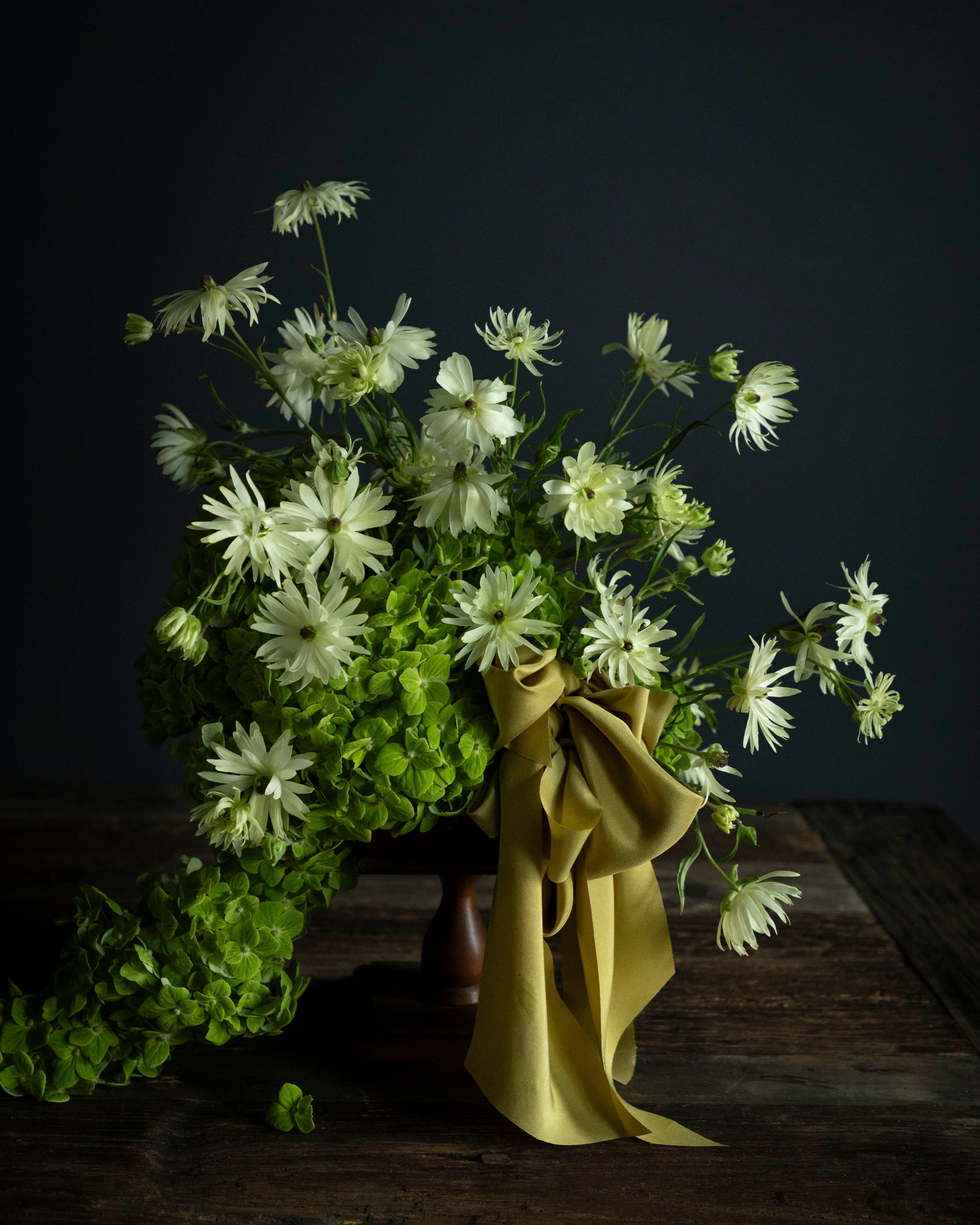 Bouquet of white flowers with greenery on a dark background. A cirtus green ribbon bow adorns the arrangement