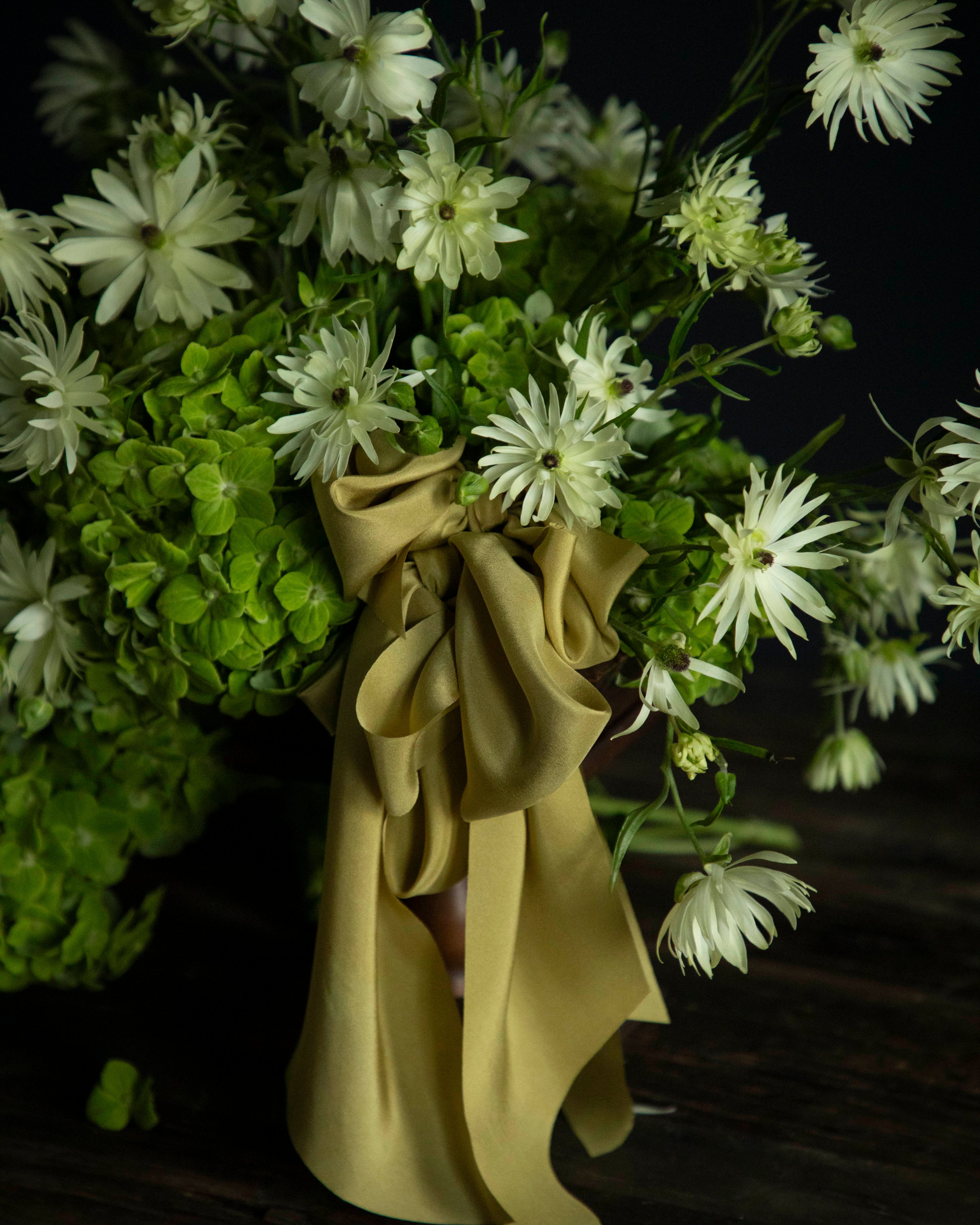 Bouquet of green and white flowers with a Chartreuse yellow ribbon on a dark background