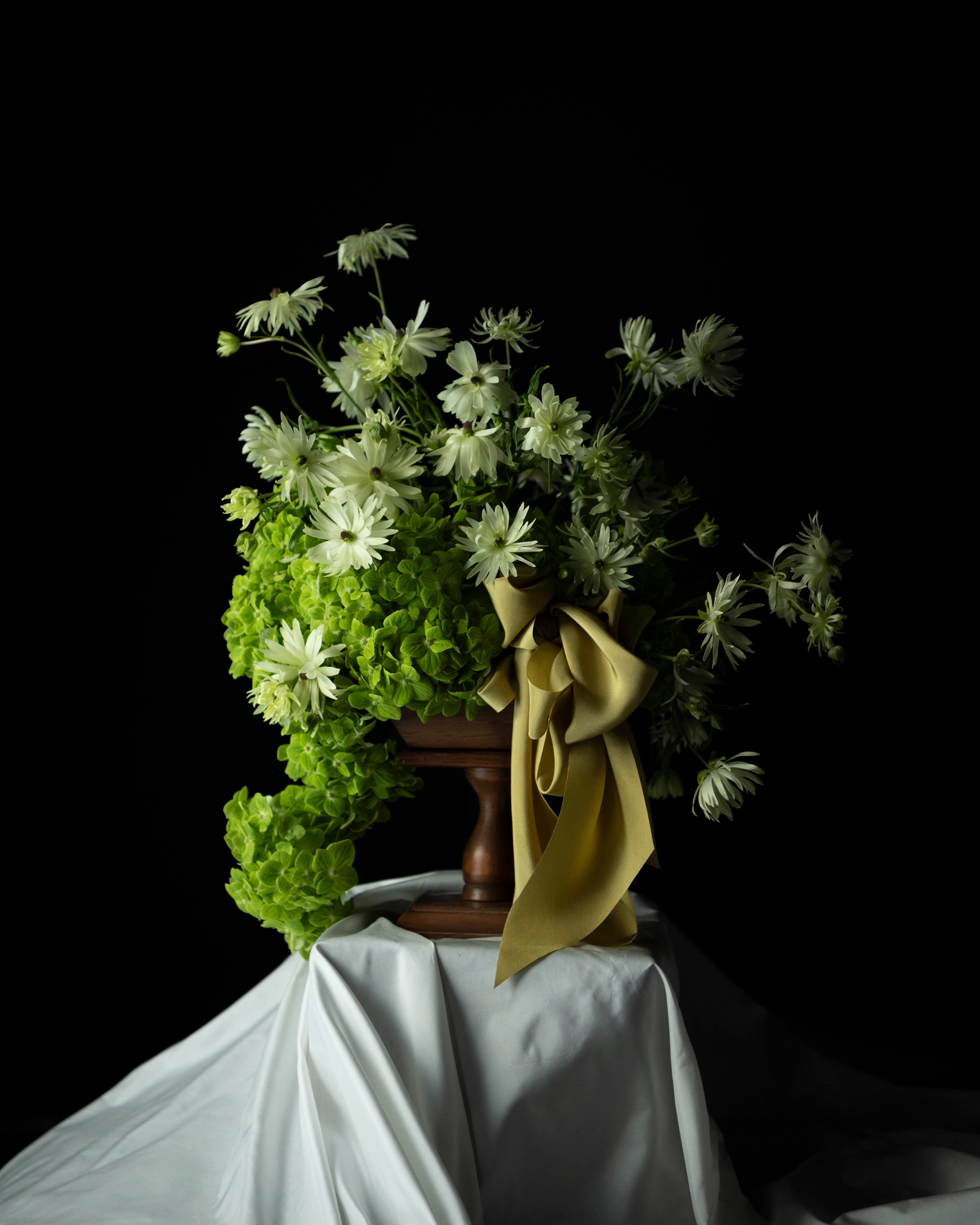 Bouquet of flowers with a green ribbon on a white tablecloth against a black background