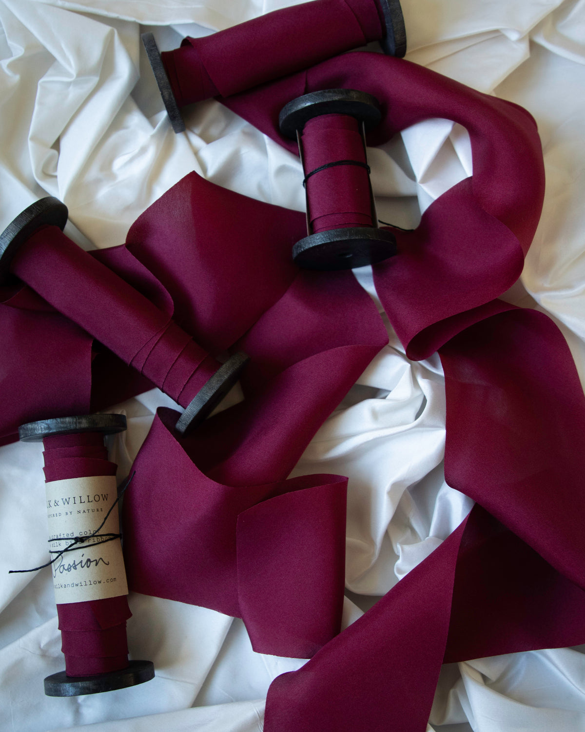 Passion red silk ribbon on wood spools on a white background.