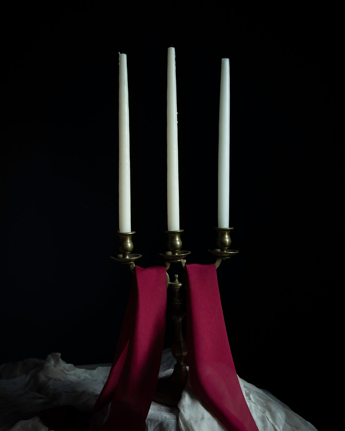 brass candelabra with candles and draping red silk ribbons against a dark background.