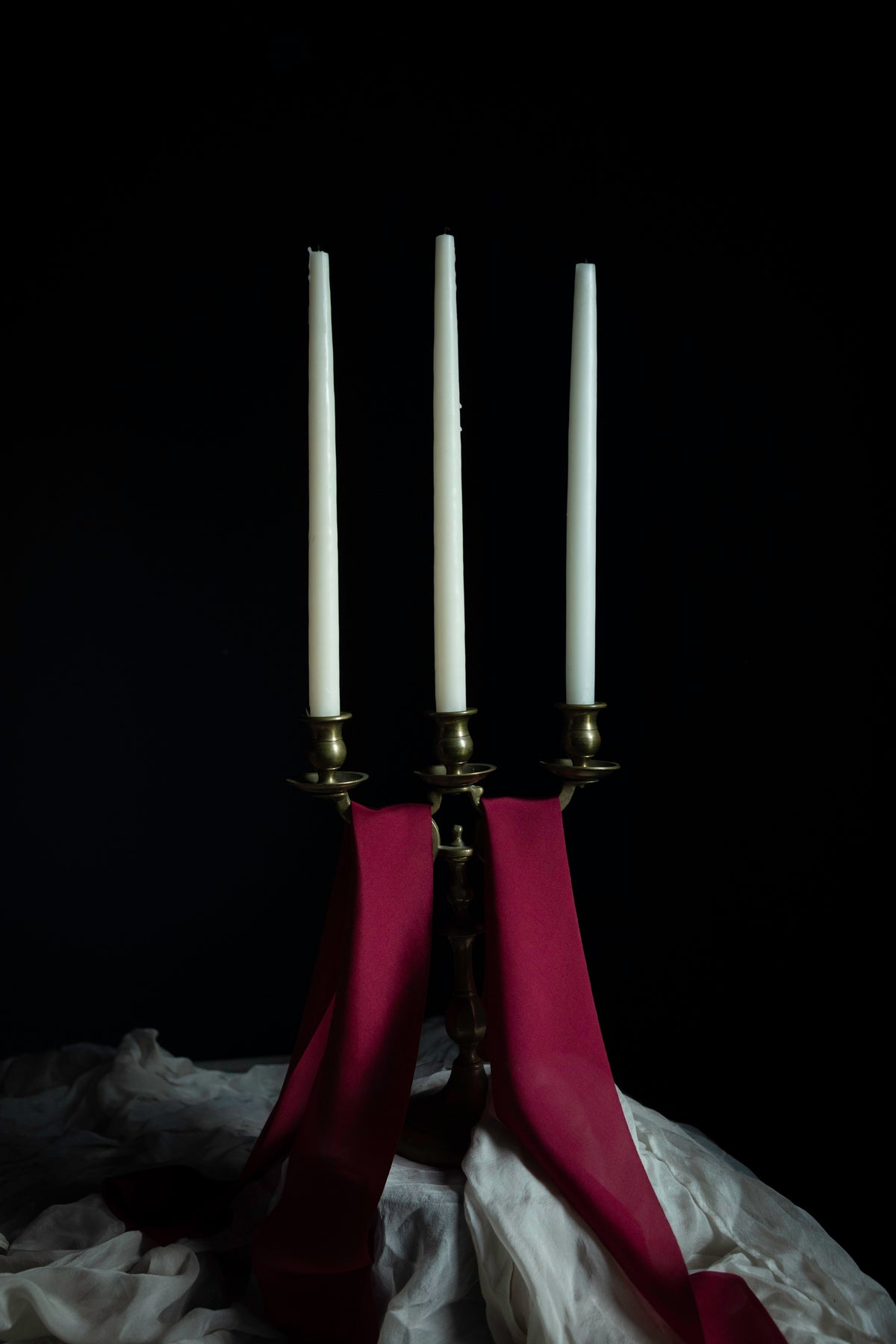brass candelabra with candles and draping red silk ribbons against a dark background.