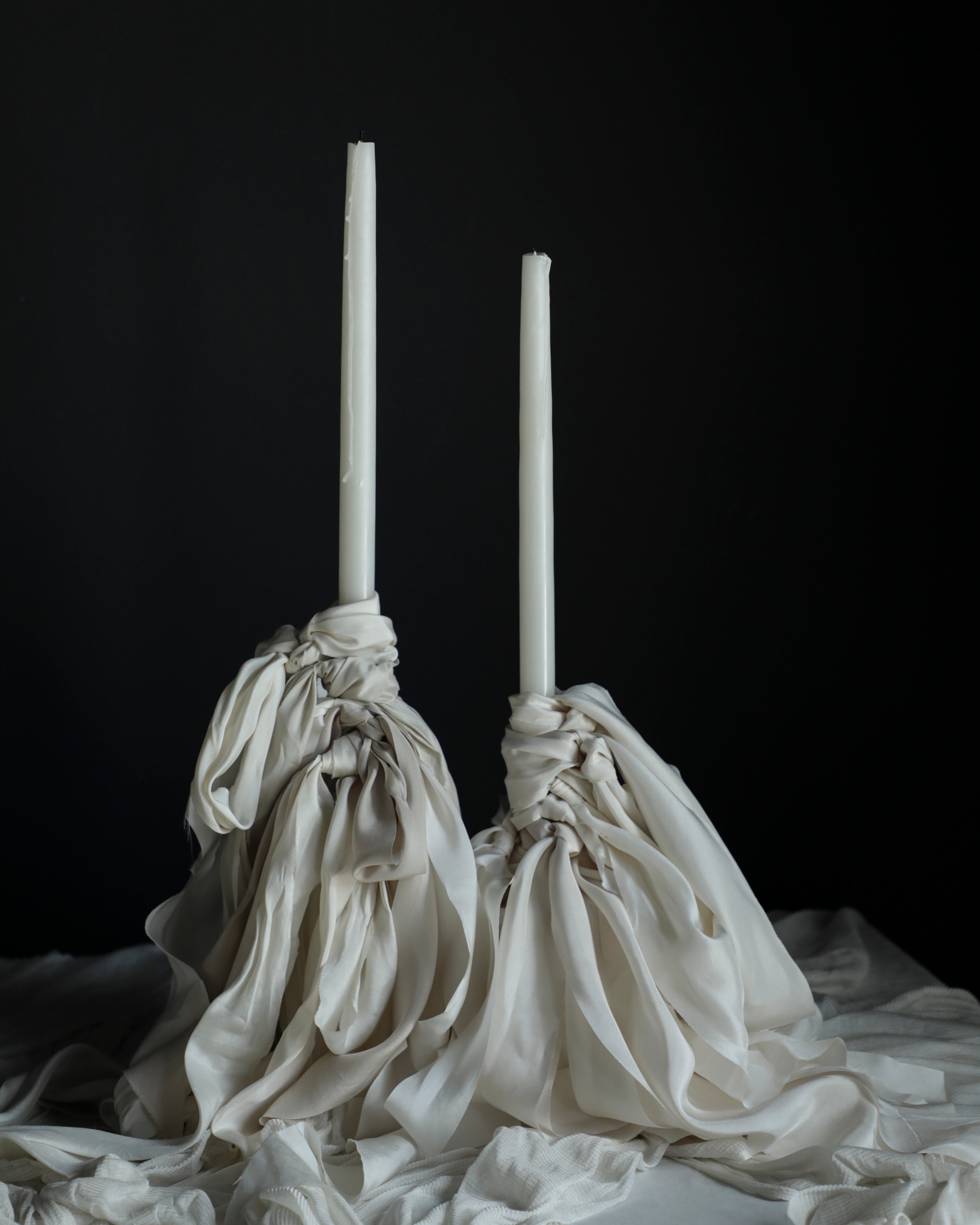 Two white candles in decorative cloth holders on a dark background