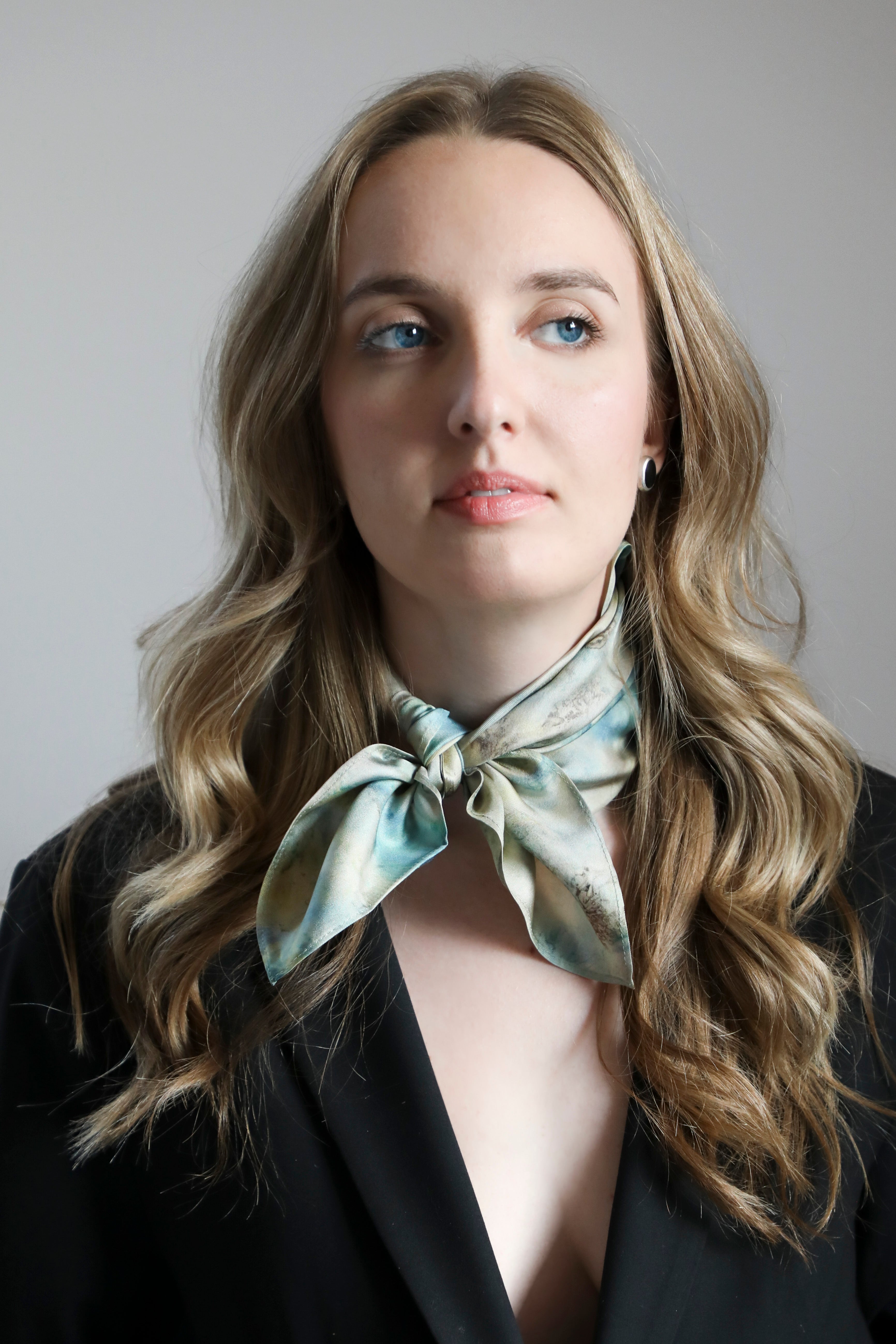 A pure silk scarf with a botanical print, featuring shades of blue, teal, and creamy gold colors, displayed on a dark background.