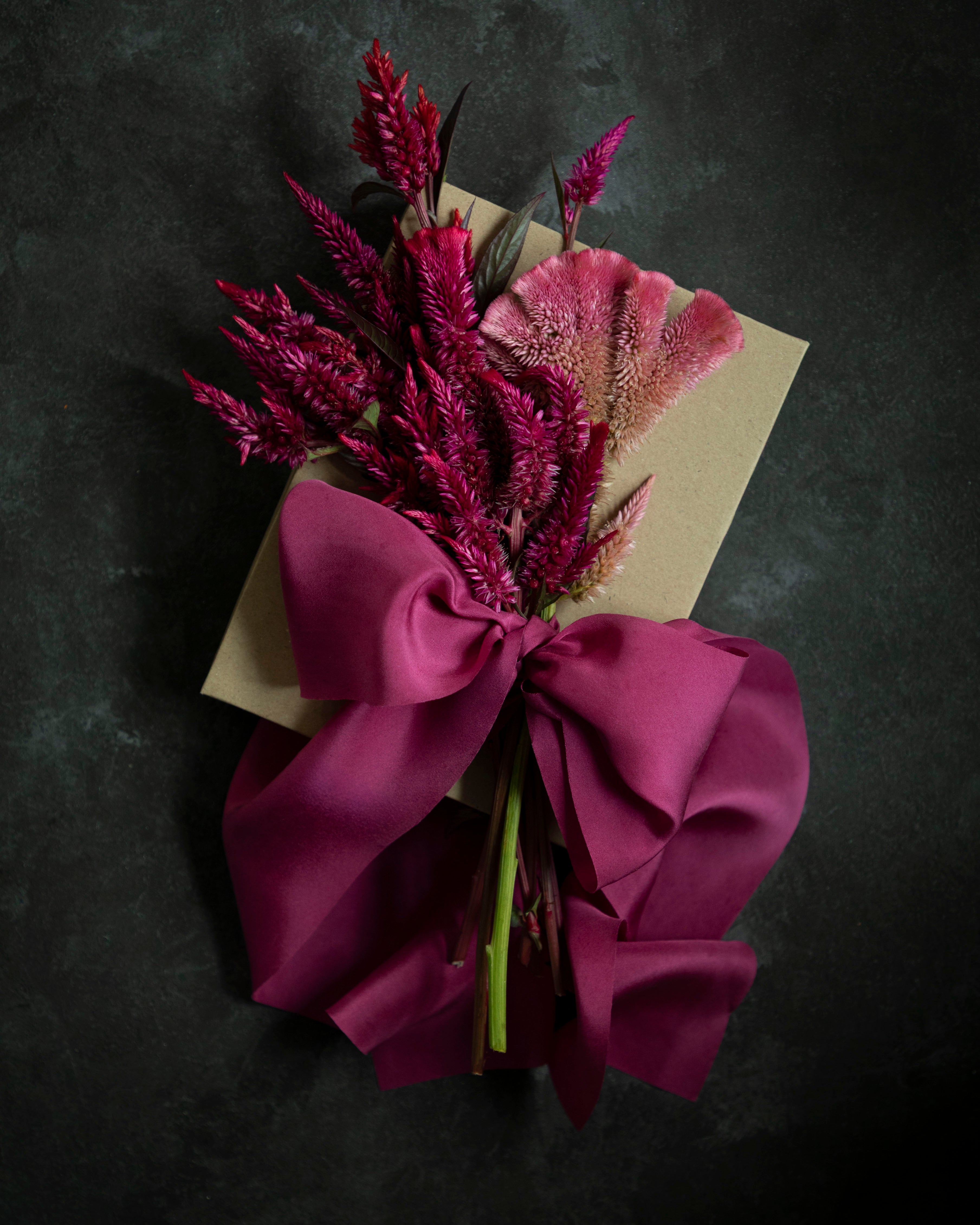 Bouquet of purple flowers with a large pink bow on a dark background