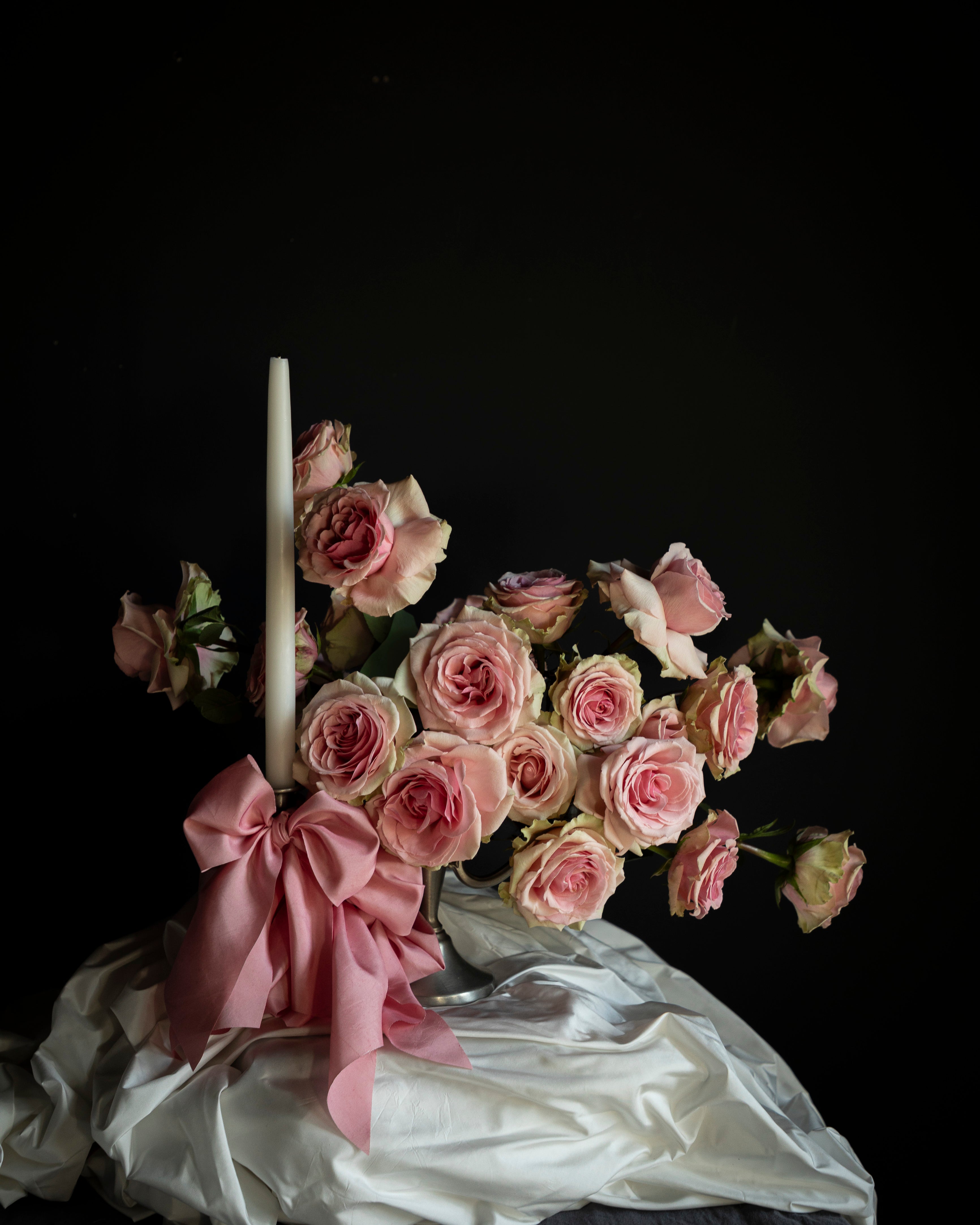 Bouquet of pink roses with a candle and pink ribbon on a dark background