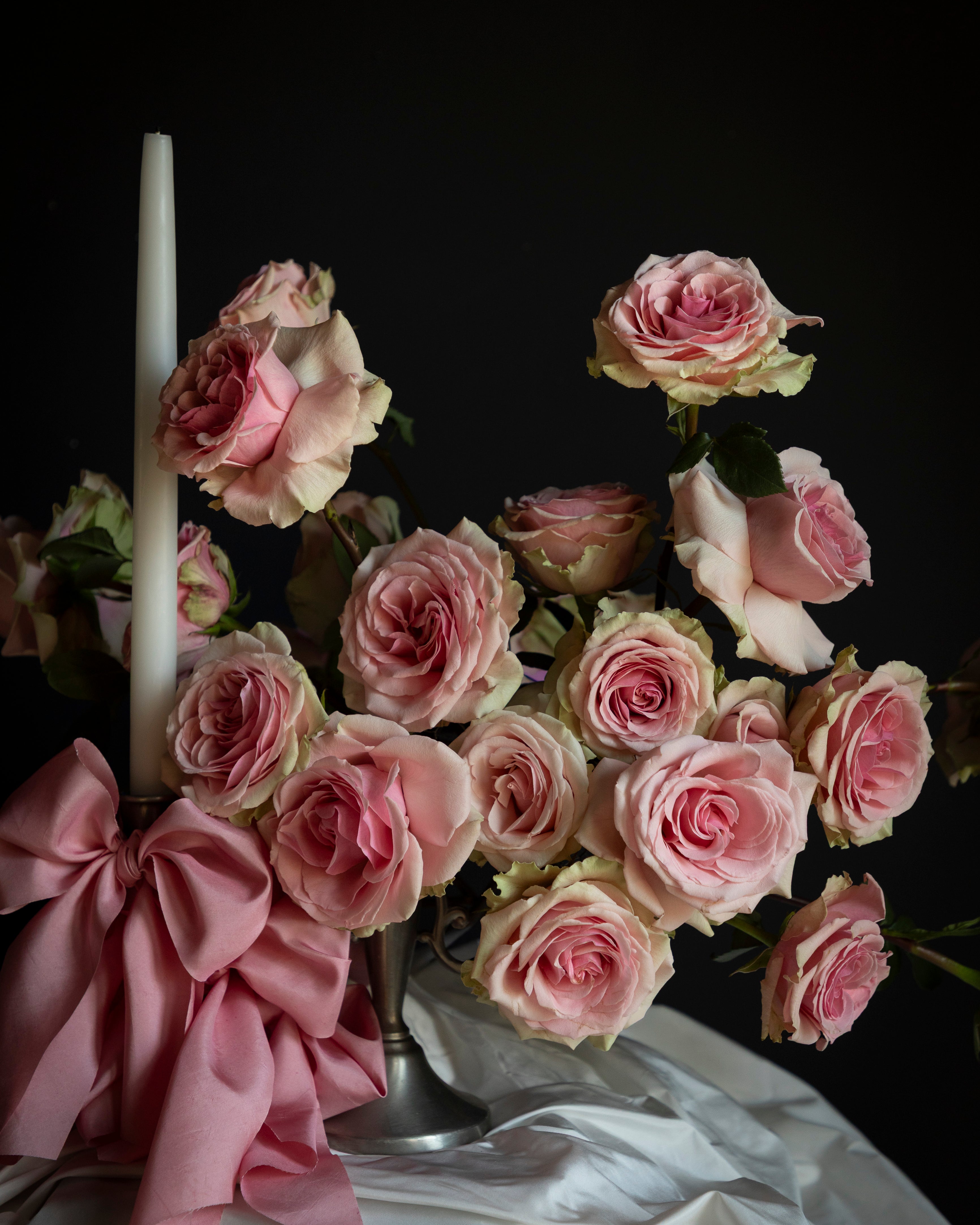 Bouquet of pink roses with a white candle and pink ribbon on a dark background