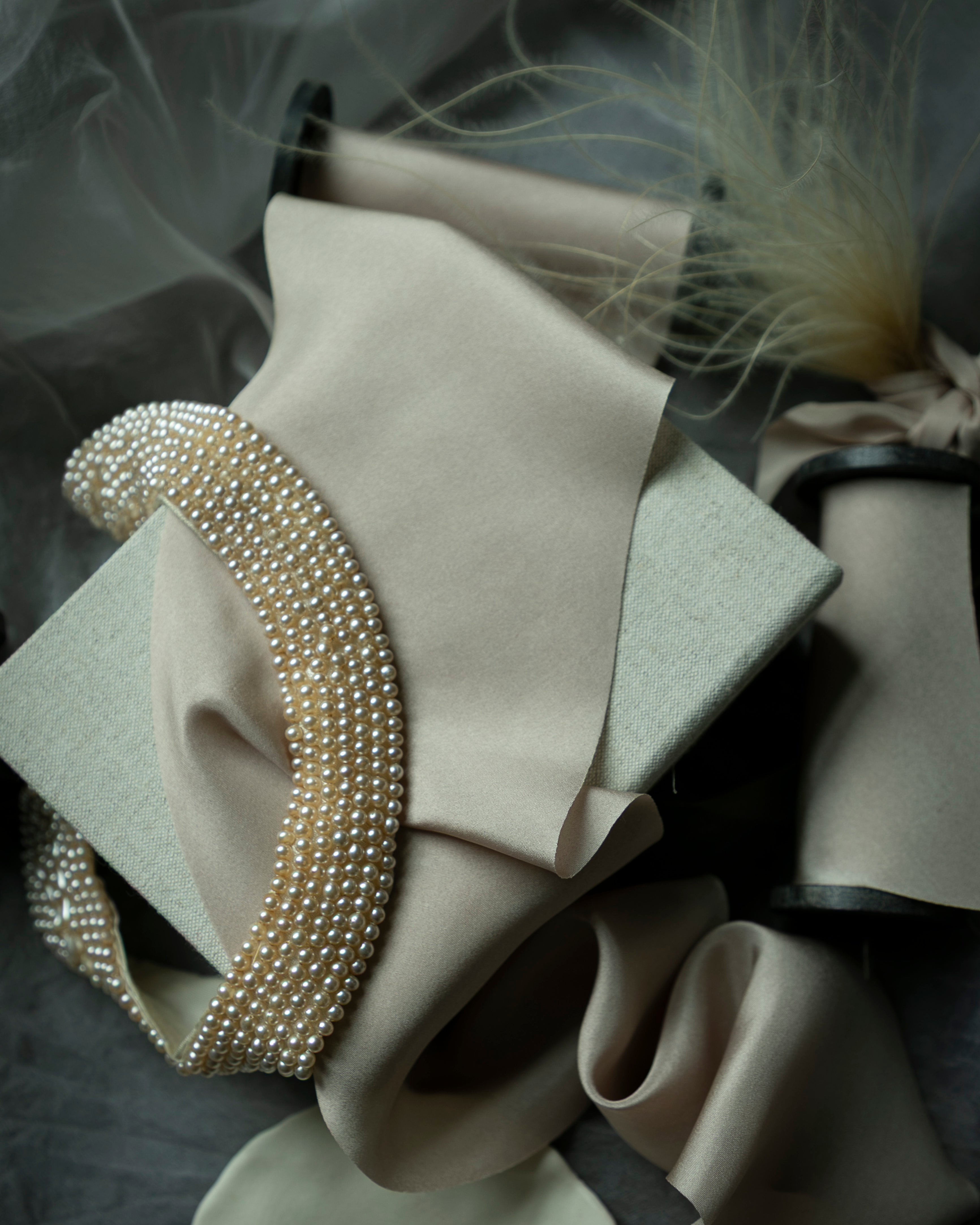 Pearl-colored silk ribbon on display with vintage pearls and feathers