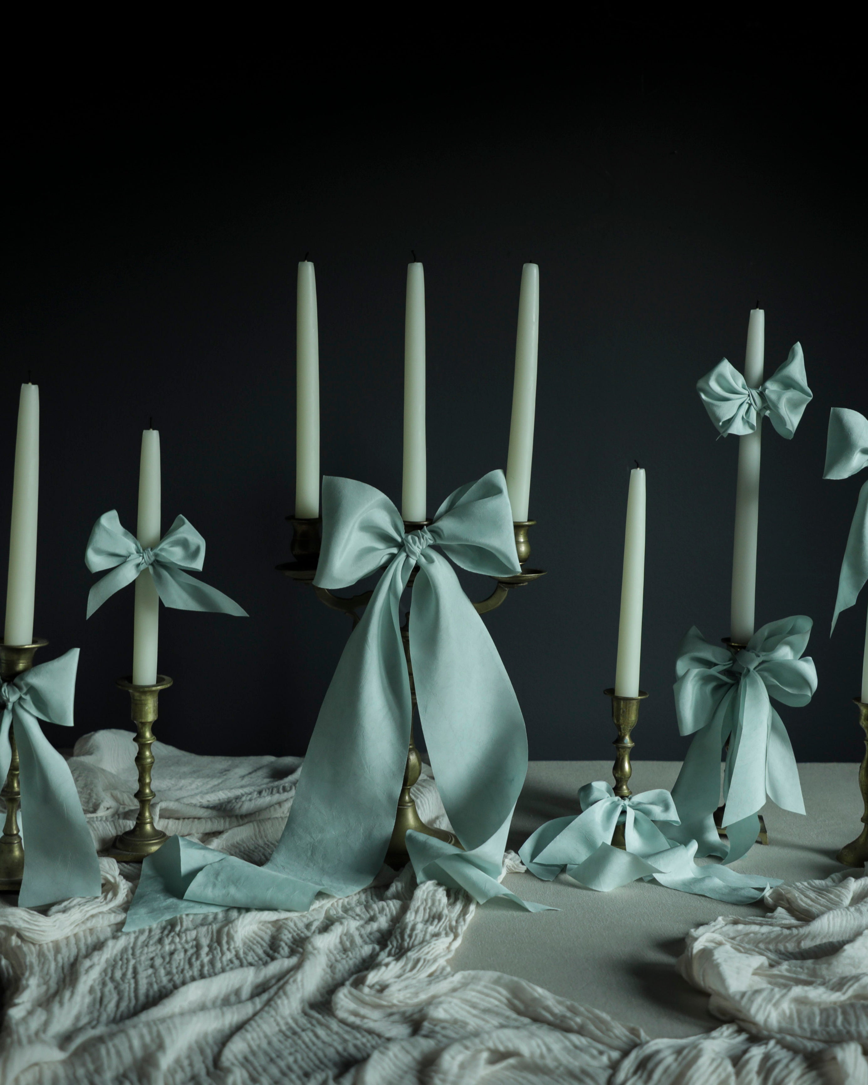 Decorative candles on a wedding tablescape design with ribbons on a dark background