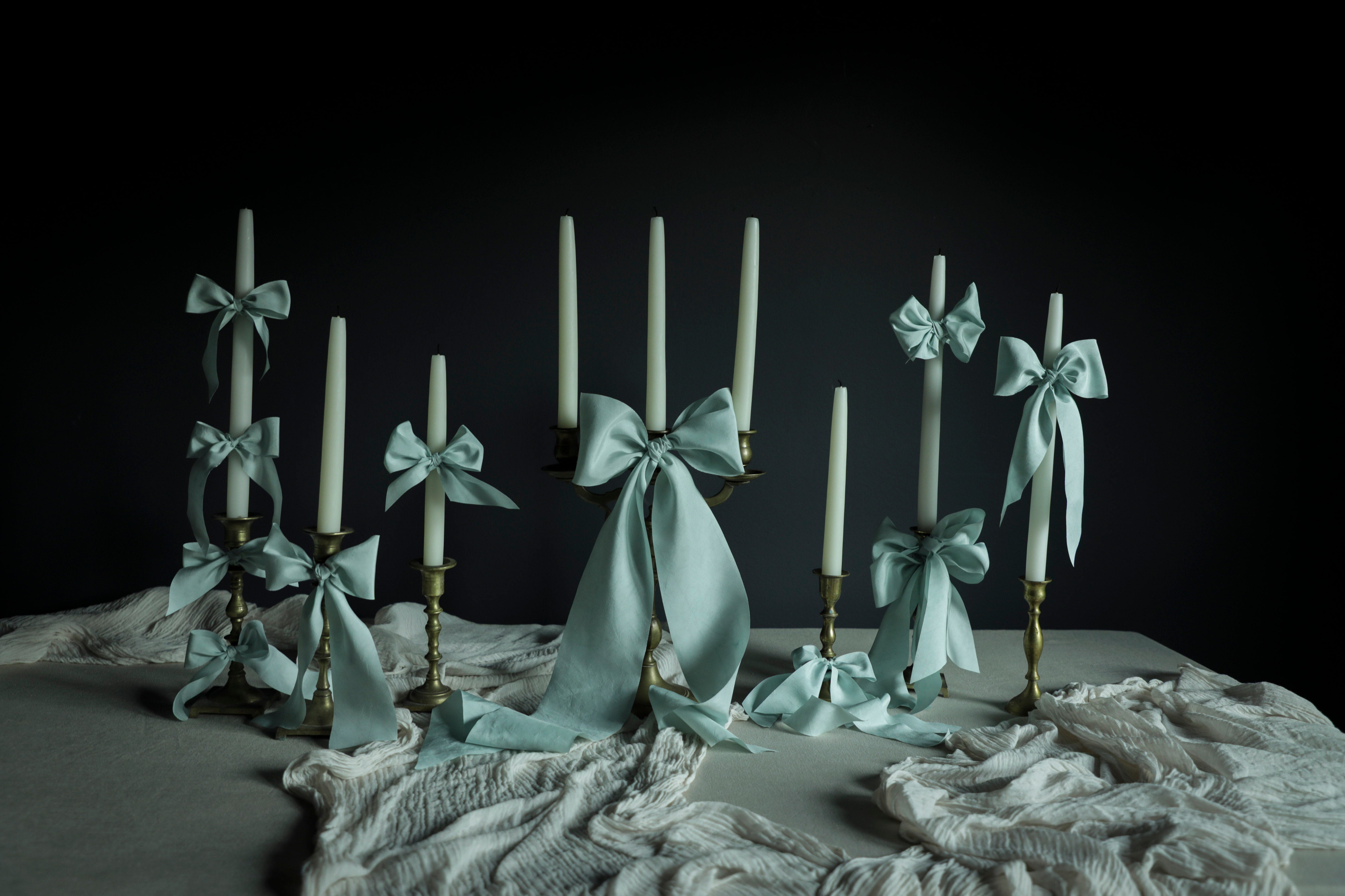 Decorative candles on a wedding tablescape design with ribbons on a dark background