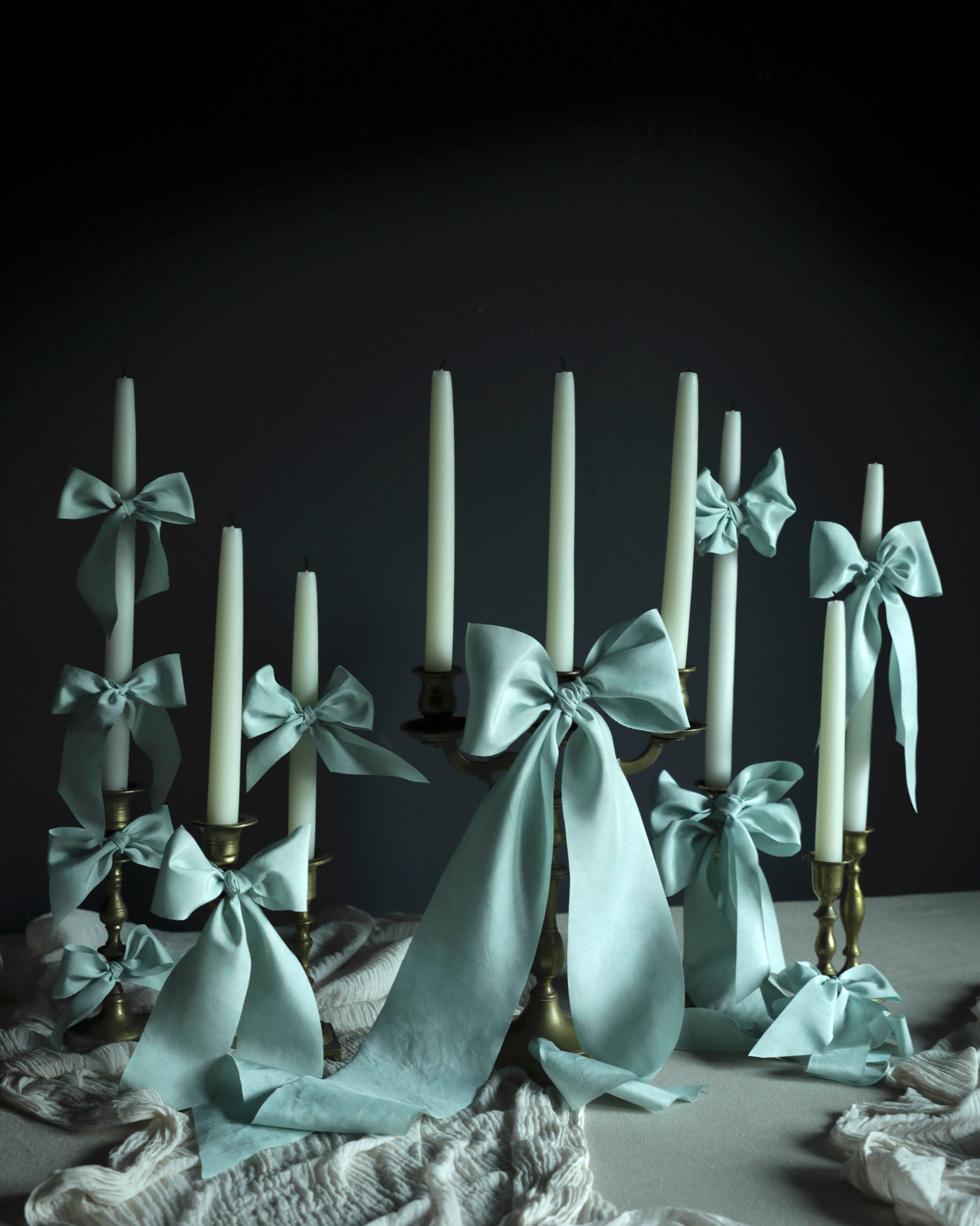 Candlesticks with white candles and light blue ribbons on a dark background