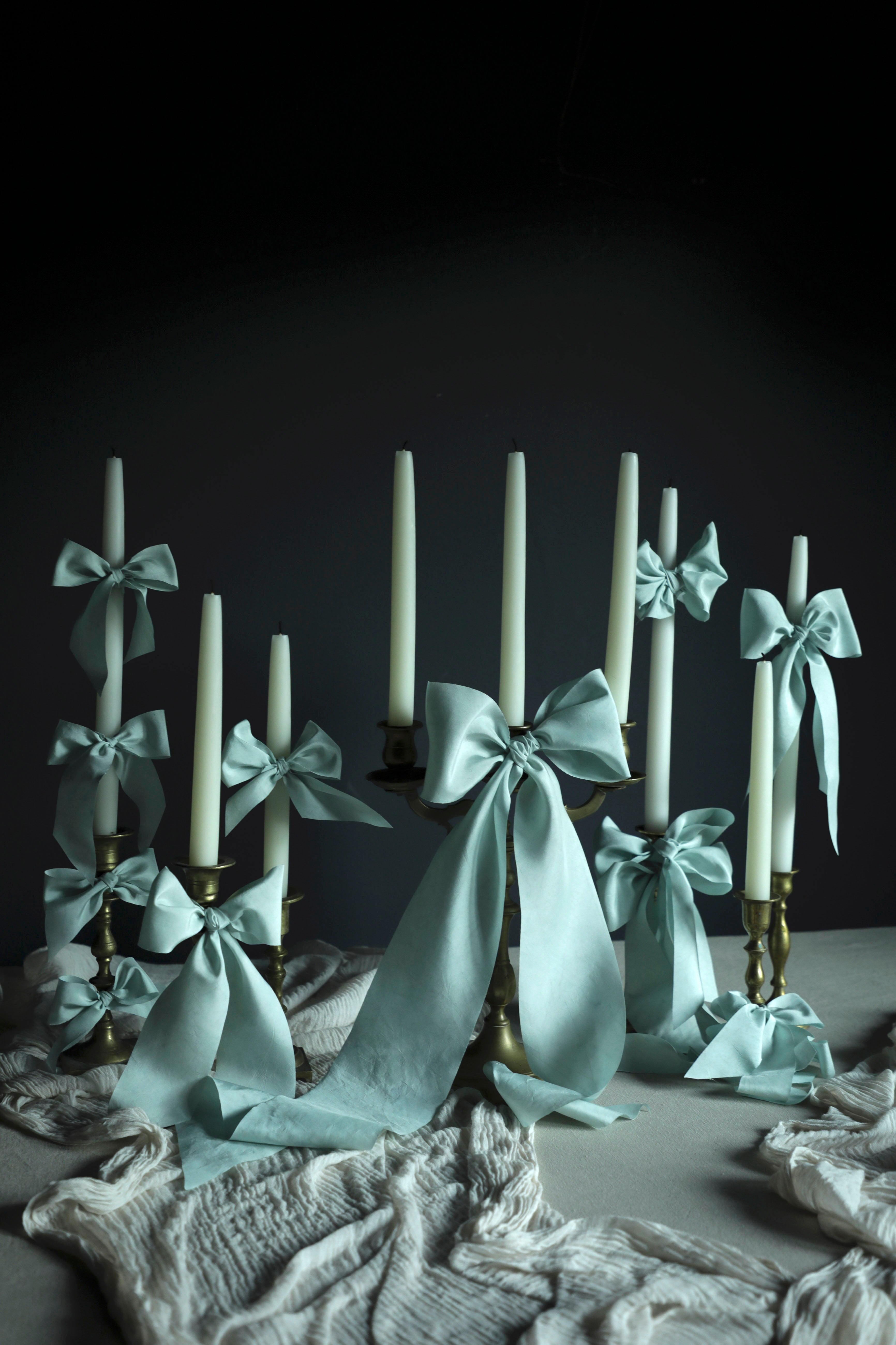 Candlesticks with white candles and light blue ribbons on a dark background