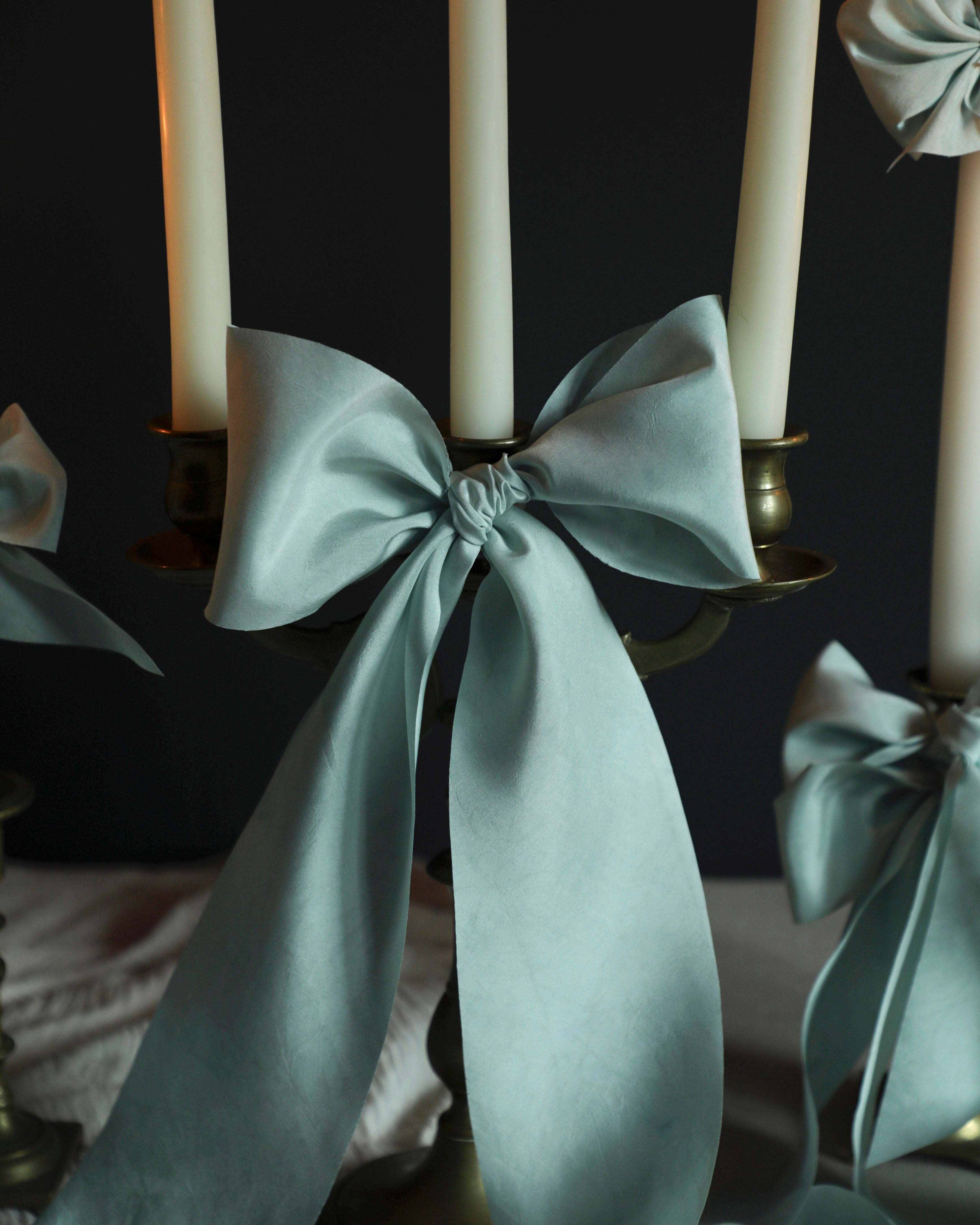 Candle holder with light indigo blue silk ribbons and candles against a dark background