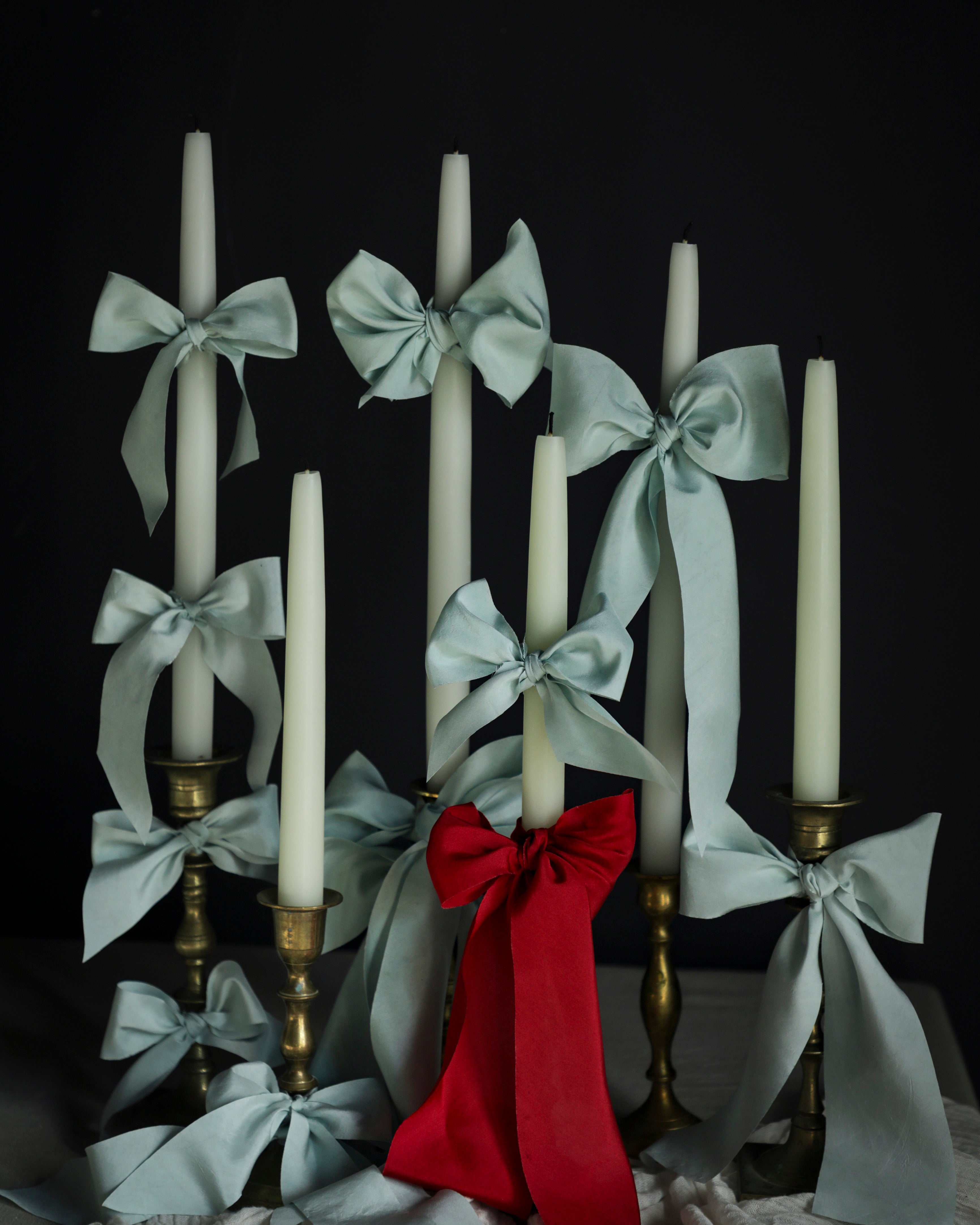 Candle holder with white candles, Cinderella blue silk ribbons, and a red bow on a dark background