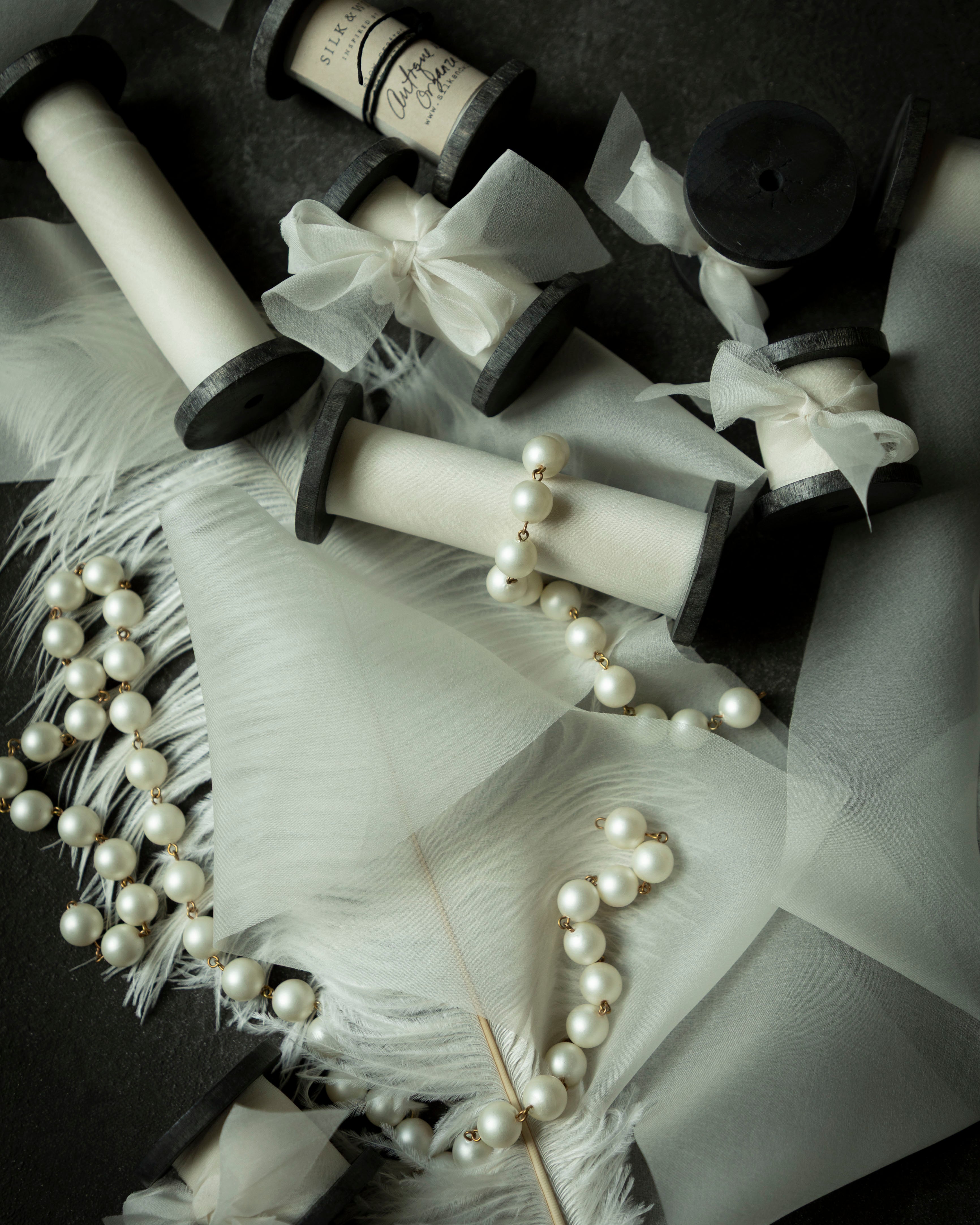 antique white wedding ribbon for florists. Displayed on a flatlay with white feather and pearls.