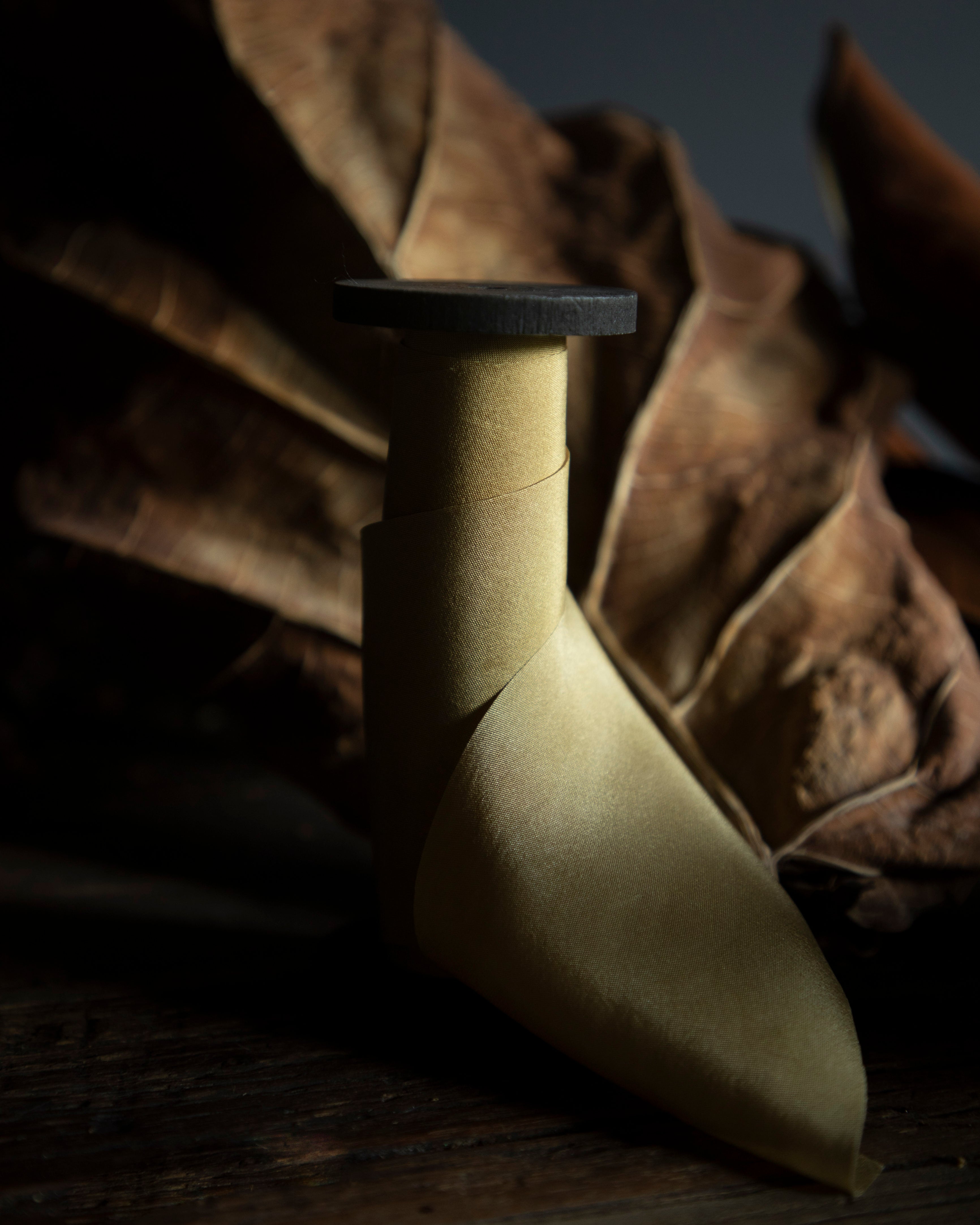 Plant-dyed silk ribbon displayed elegantly against a earthy background, showcasing its luxurious sheen and soft autumn hue, ideal for wrapping bridal bouquets. Perfect for brides-to-be, engaged couples, and florists seeking the world's finest ribbon for wedding flowers.