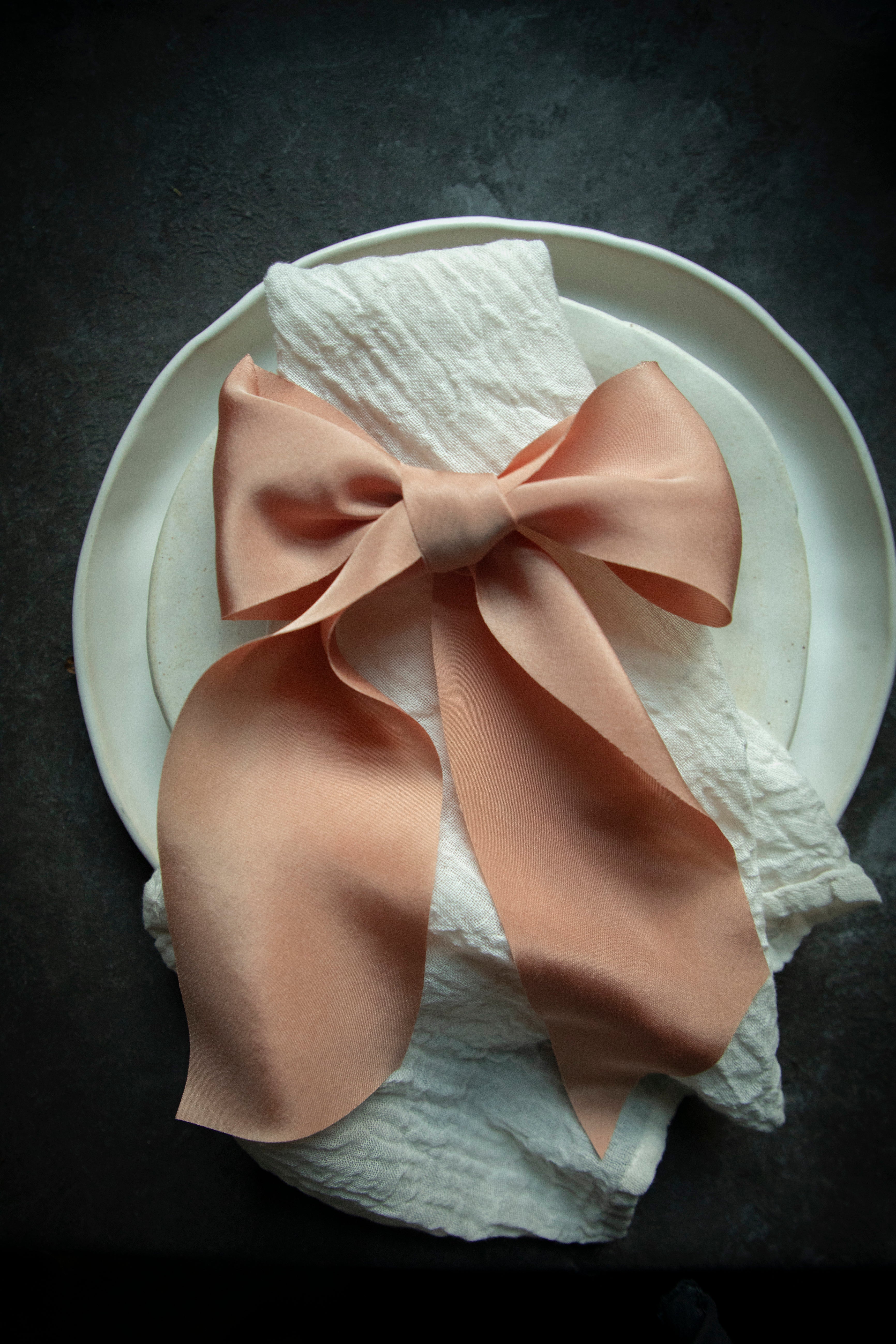 A soft coral-hued organic silk ribbon elegantly draped, showcasing its luxurious texture, ideal for adding exquisite details to wedding bouquets, invitations, and table settings.