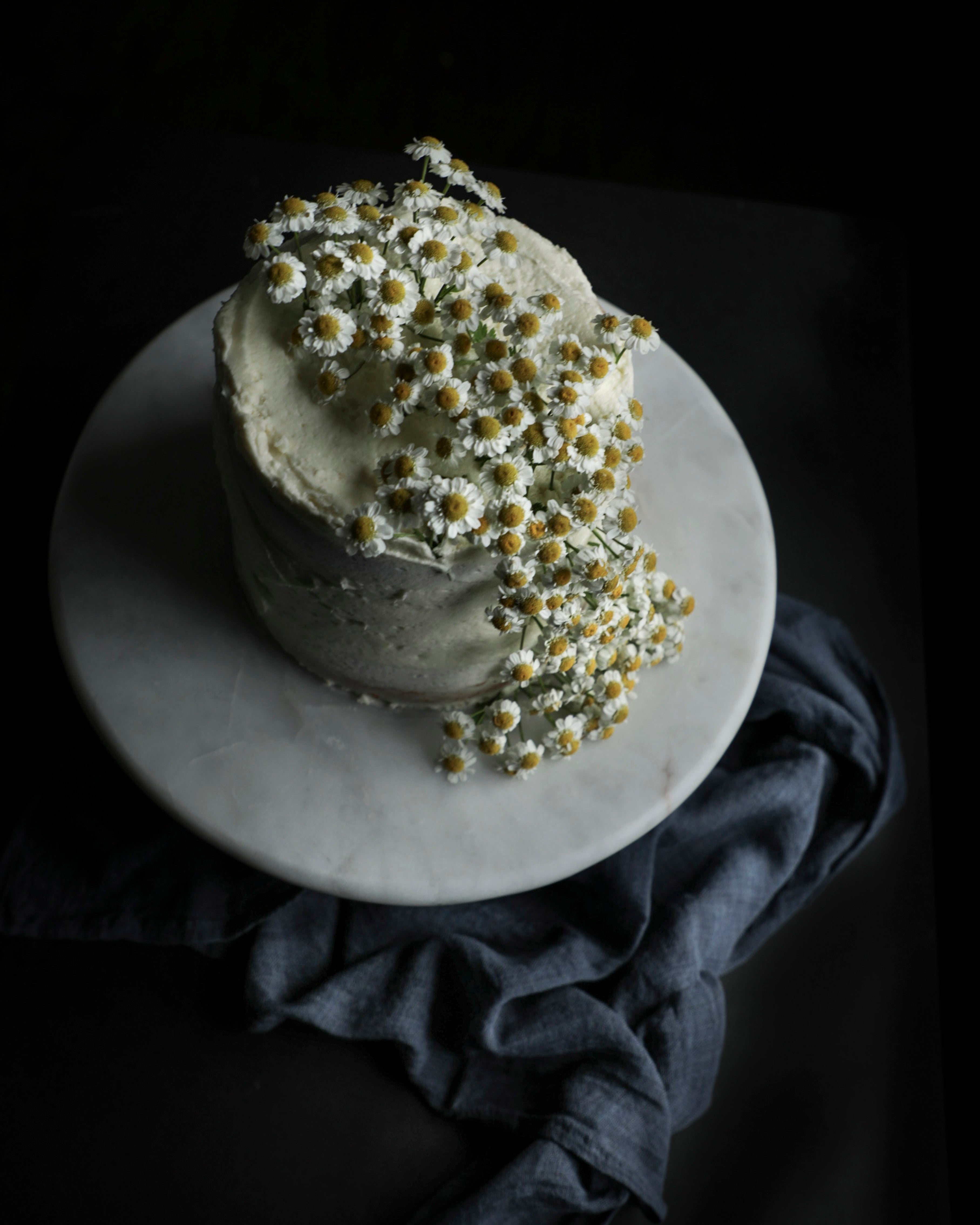 Two-tiered cake with white frosting and floral decorations on a dark background