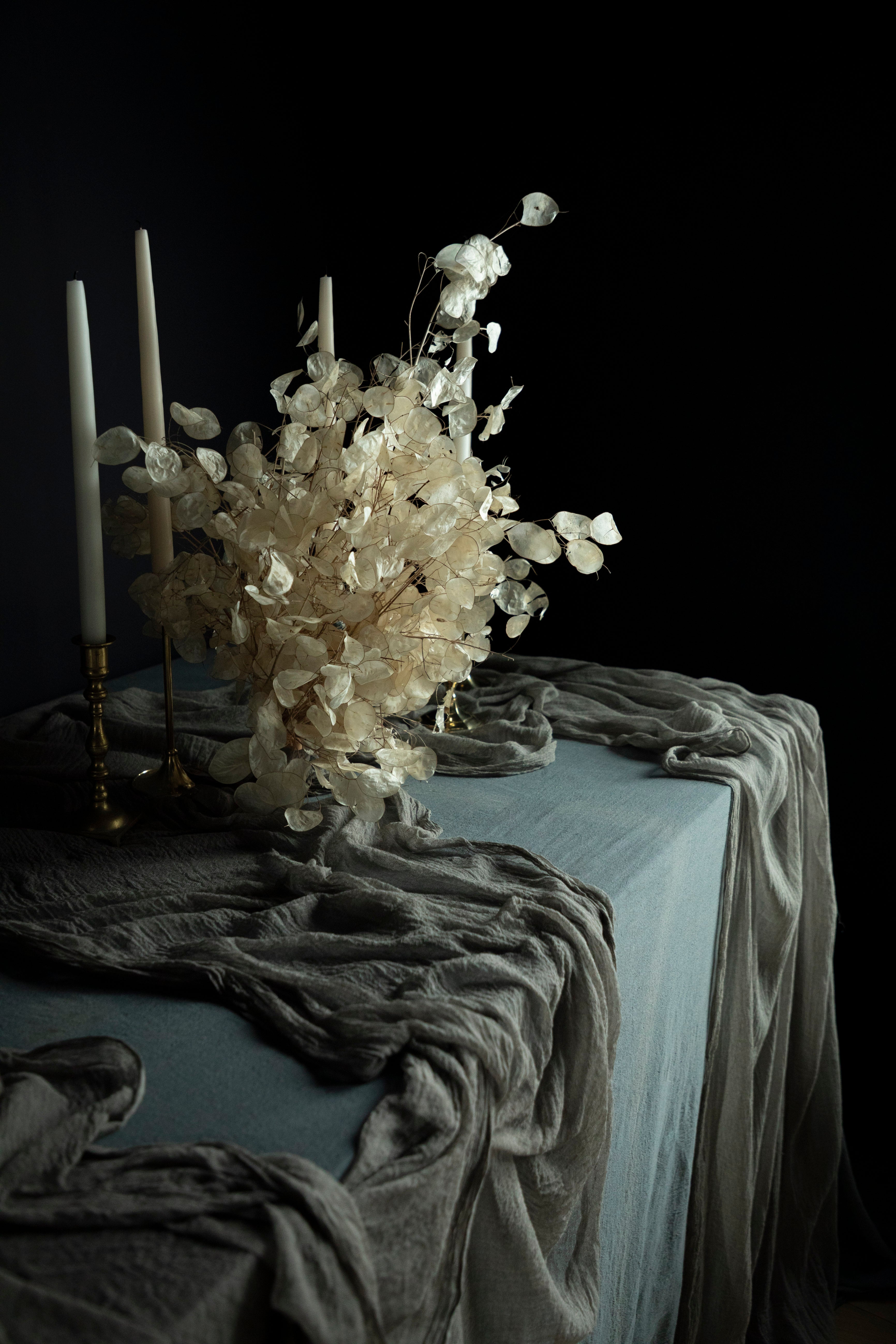 Decorative table setting with flowers, candles, and draped fabric against a dark background