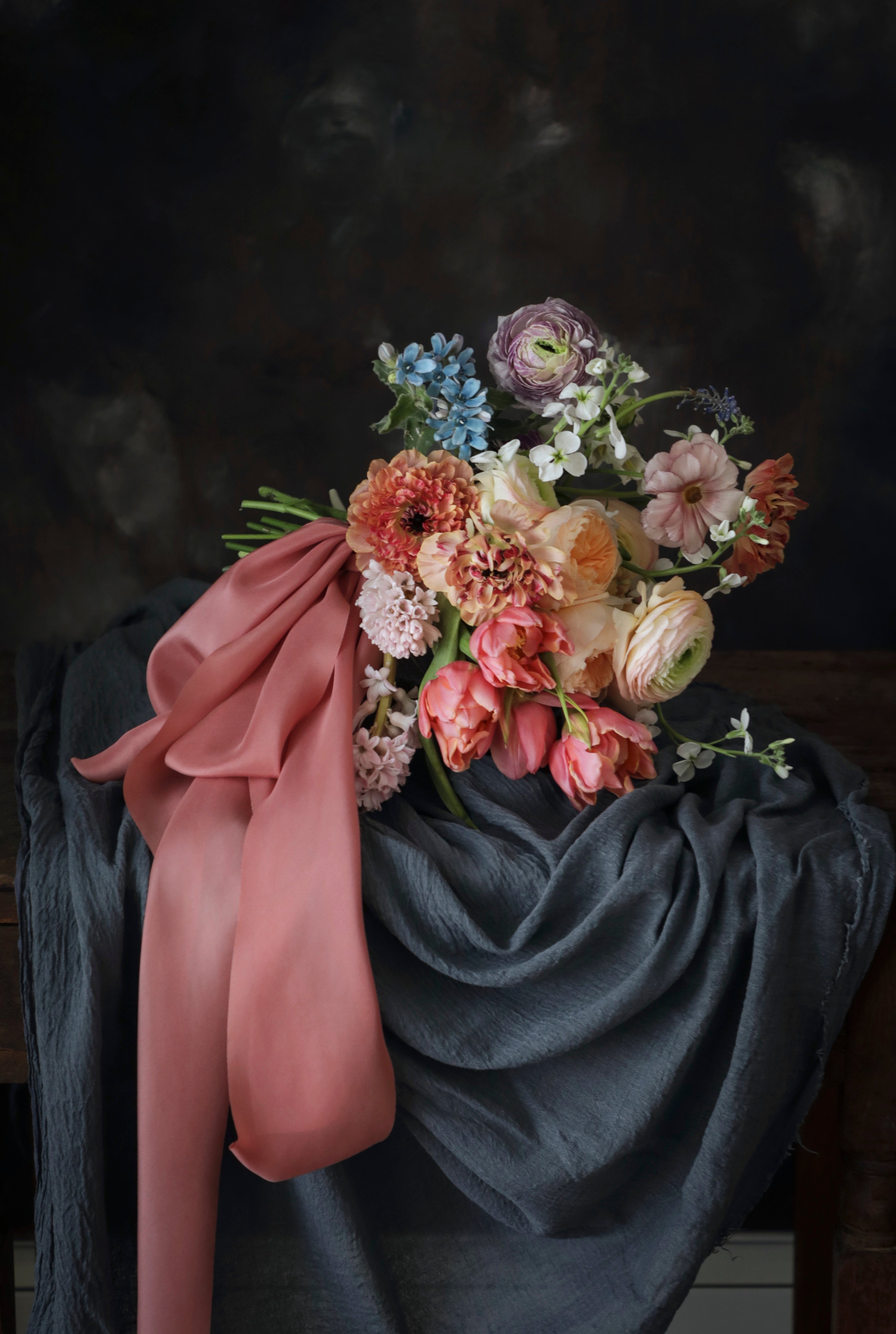 A blue slate colored table runner with a floral arrangement on top, set against a dark background.