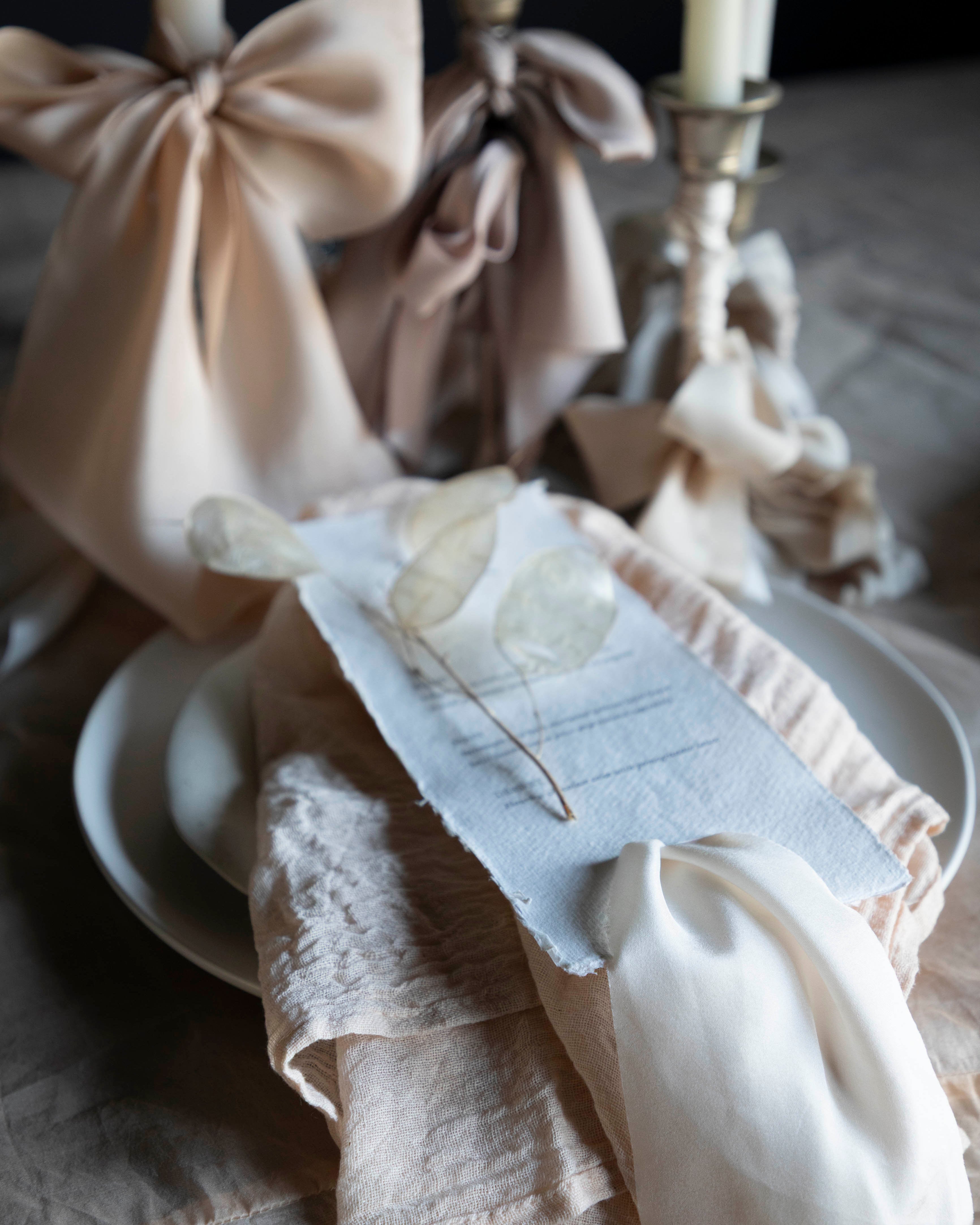 Decorative table setting with white candles, ribbons, and a small dish on a wooden surface.