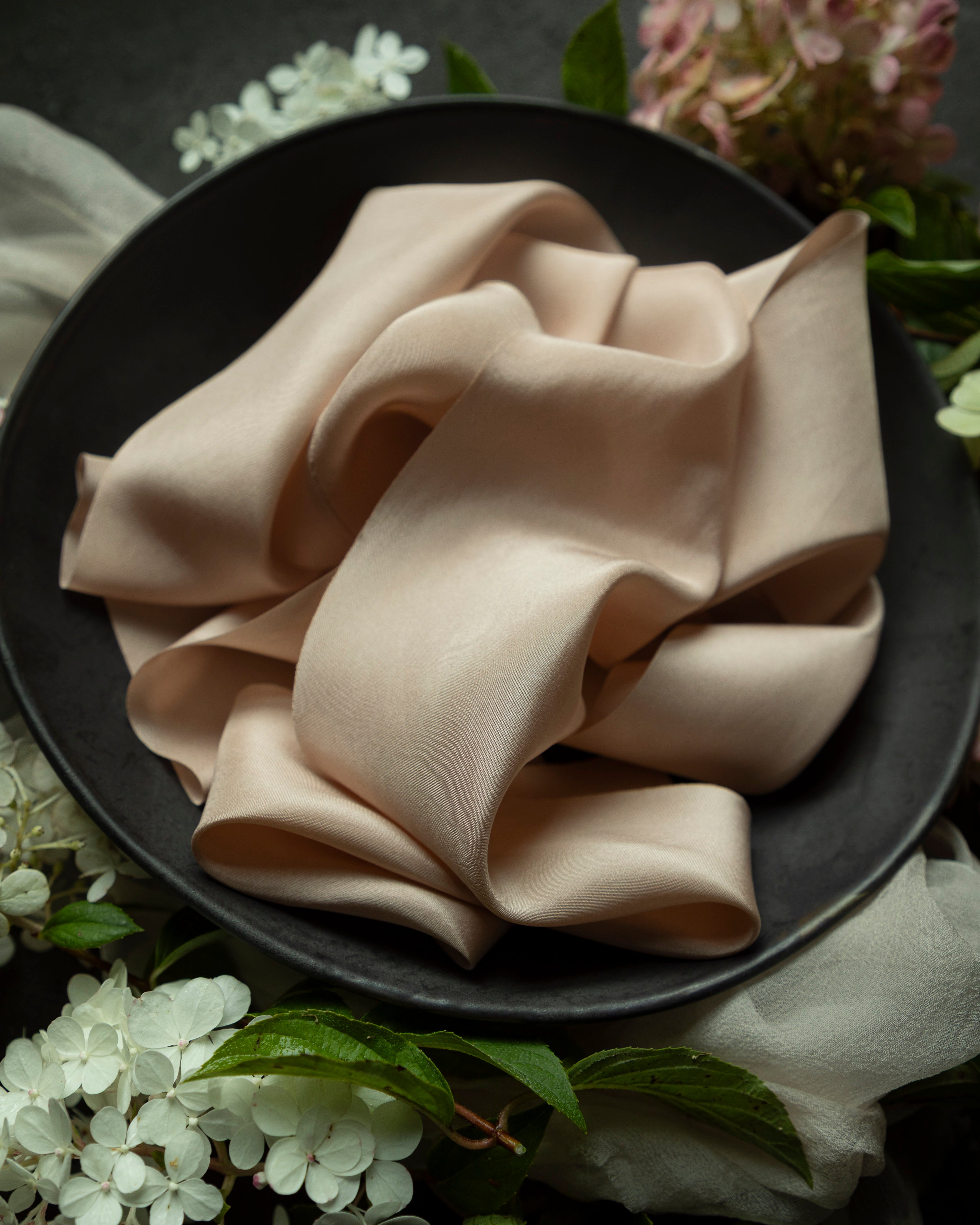Folded blush ribbon on a dark plate with floral decorations
