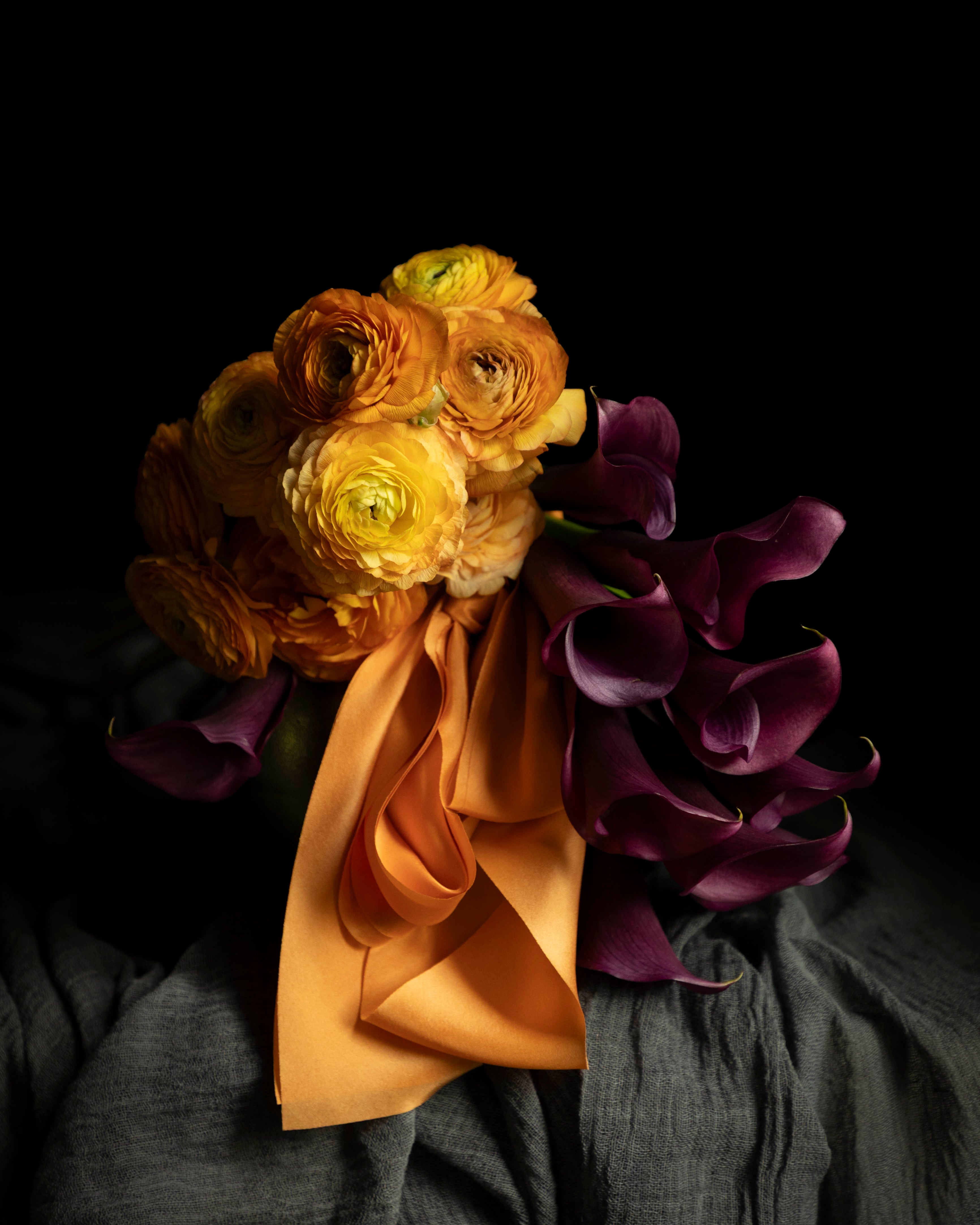 Orange ranunculus and purple calla lilies flower arrangement with orange silk ribbon