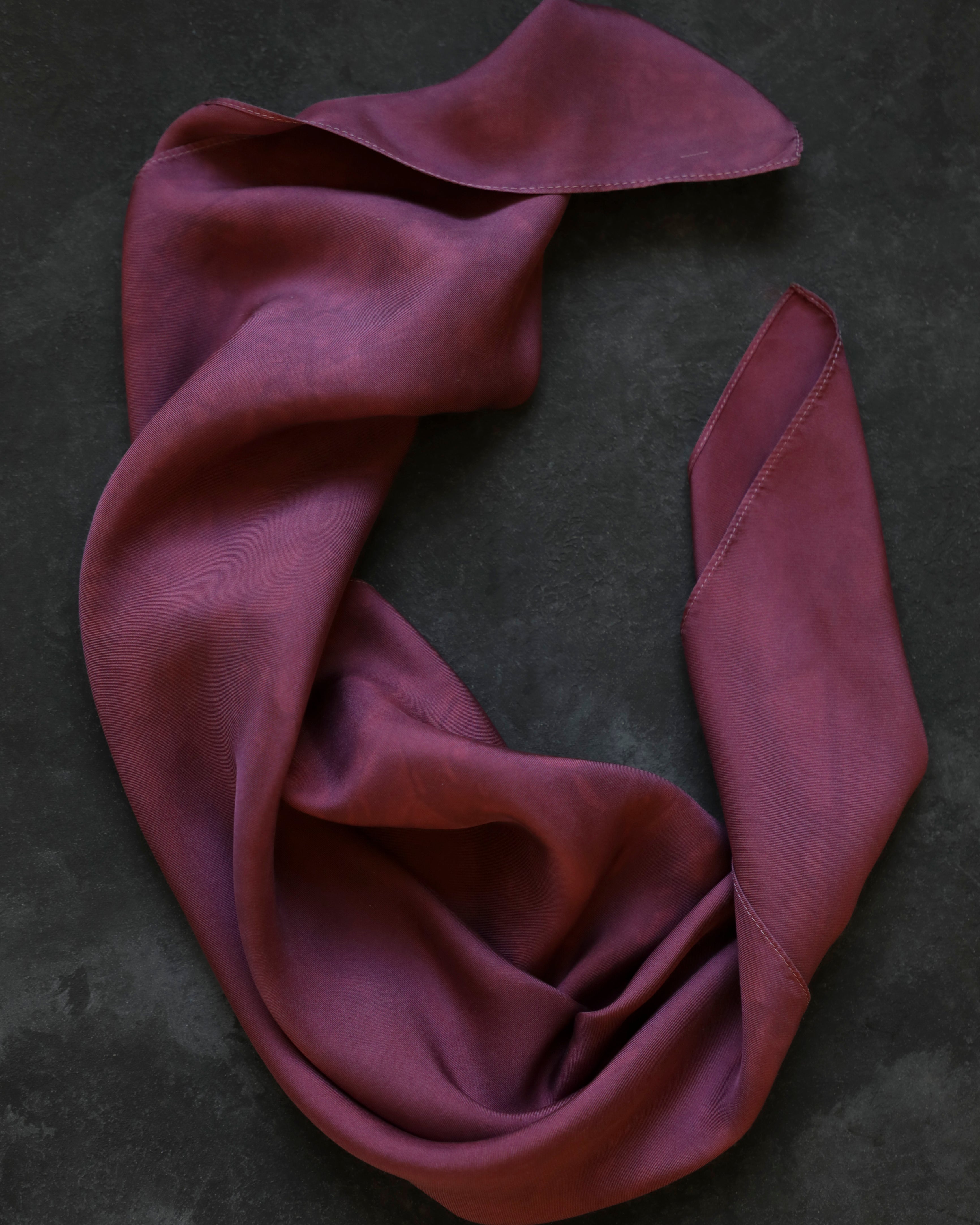 A dusty mauve-purple scarf draped in soft folds on a dark textured background.
