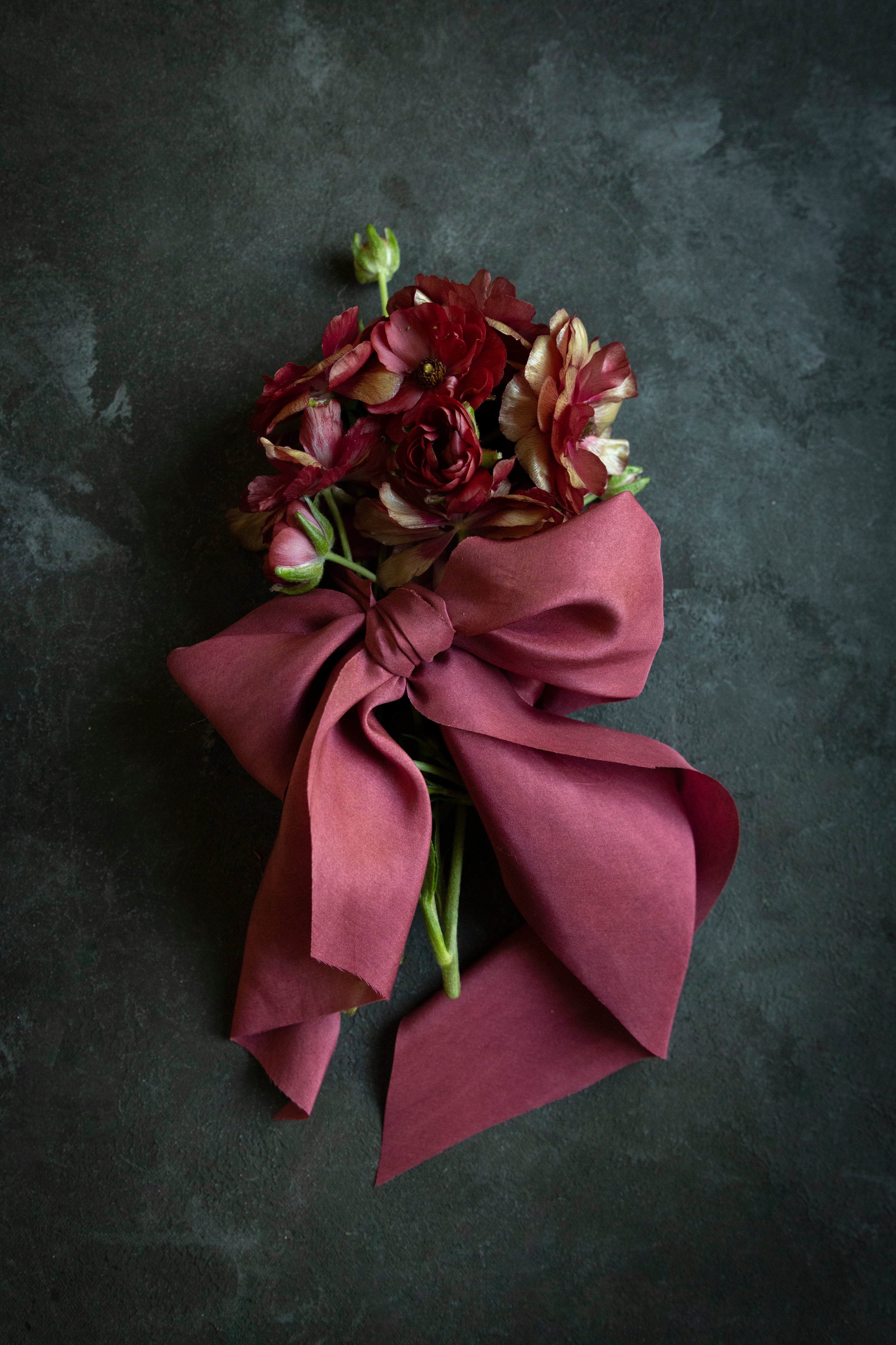 close up of flowers tied with red ribbon bow on a black surface