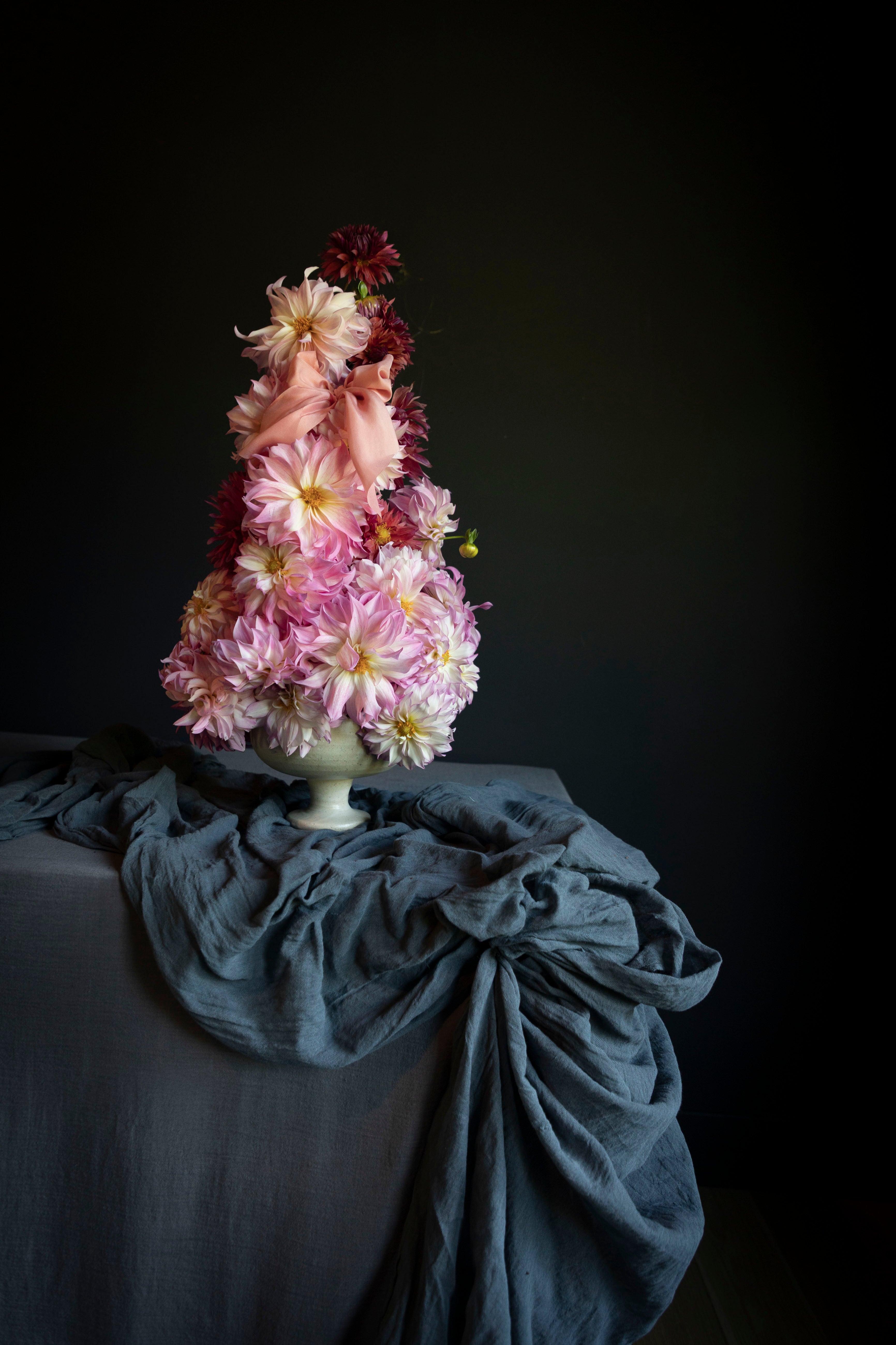 Dahlia floral arrangement on a table with styling textiles draped on the table against a dark moody background