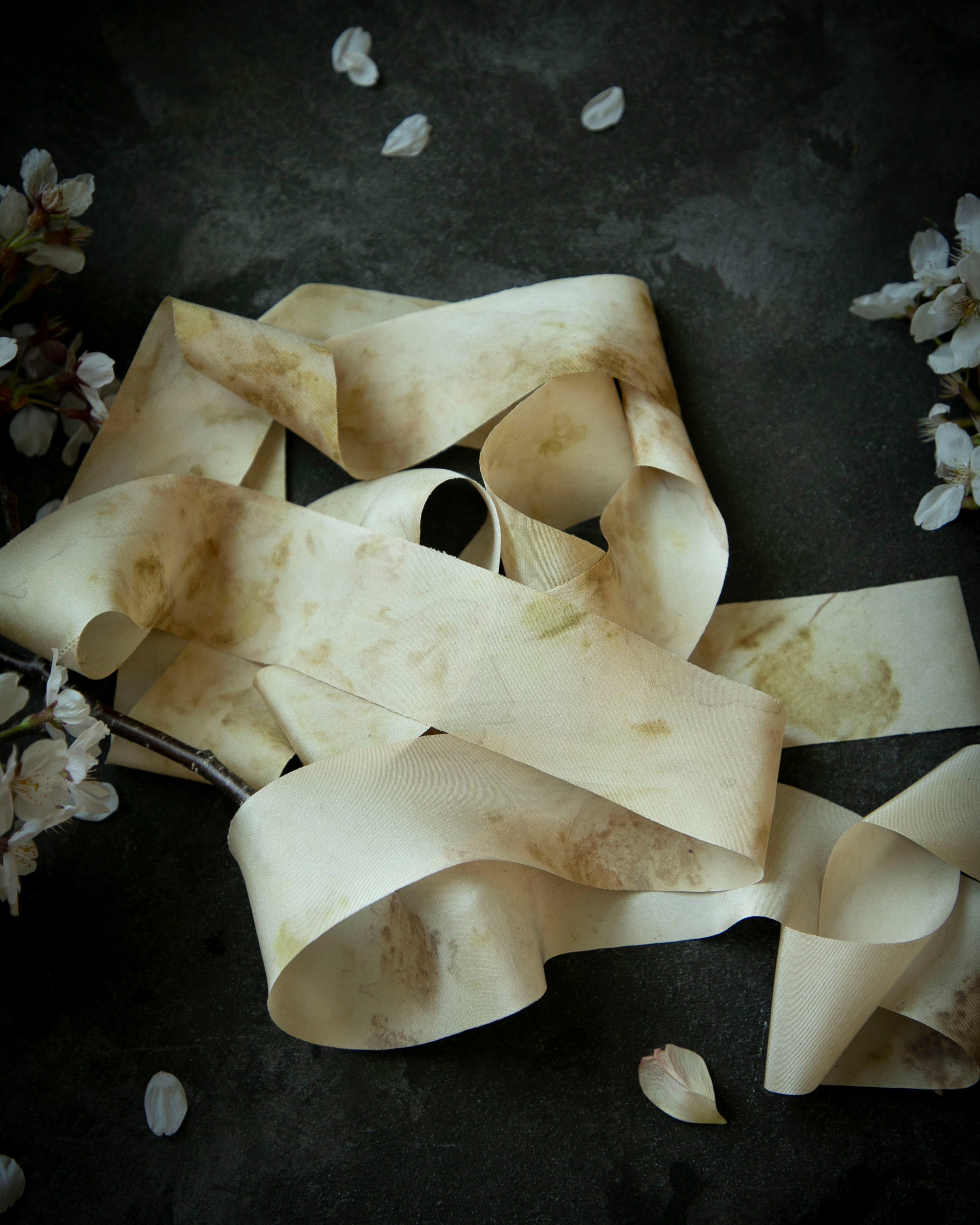 Dark textured background with eco-print silk ribbons and scattered petals on a dark background