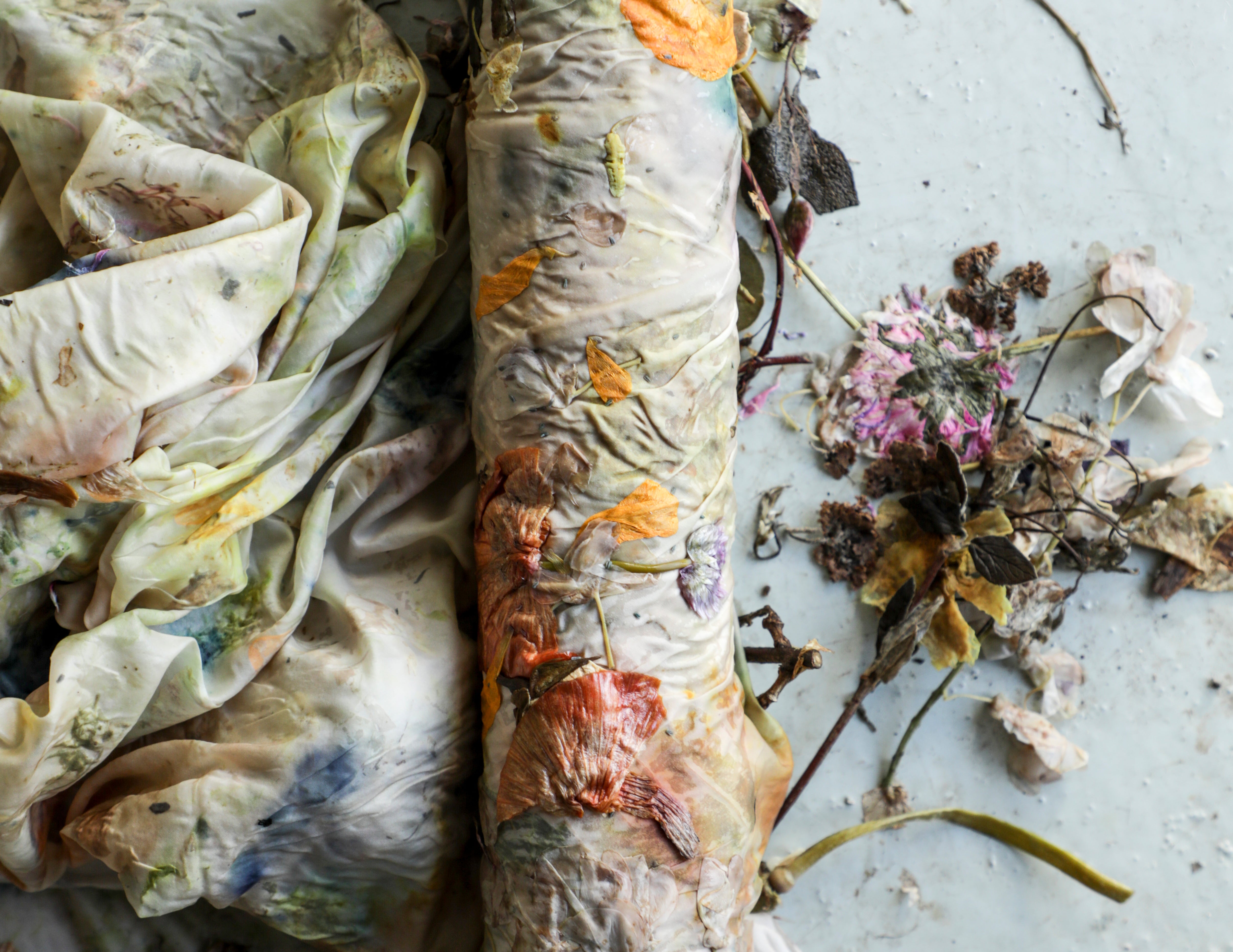 Close-up of the eco-printing technique. A close-up of flowers and plants rolled-up into silk with natural elements on a textured surface.