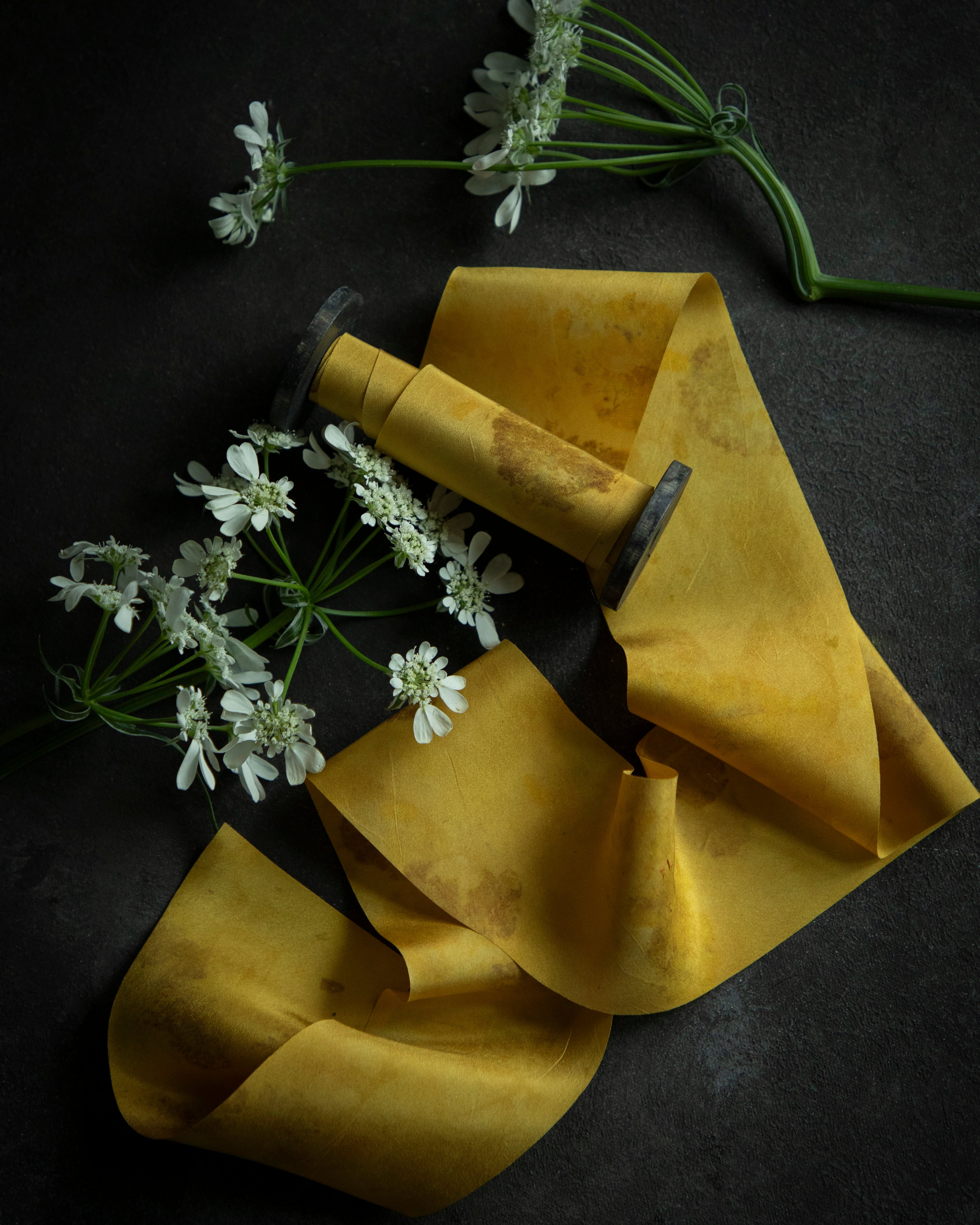 A luminous yellow silk ribbon with a floral pattern, displayed alongside fresh marigold flowers against a dark background.