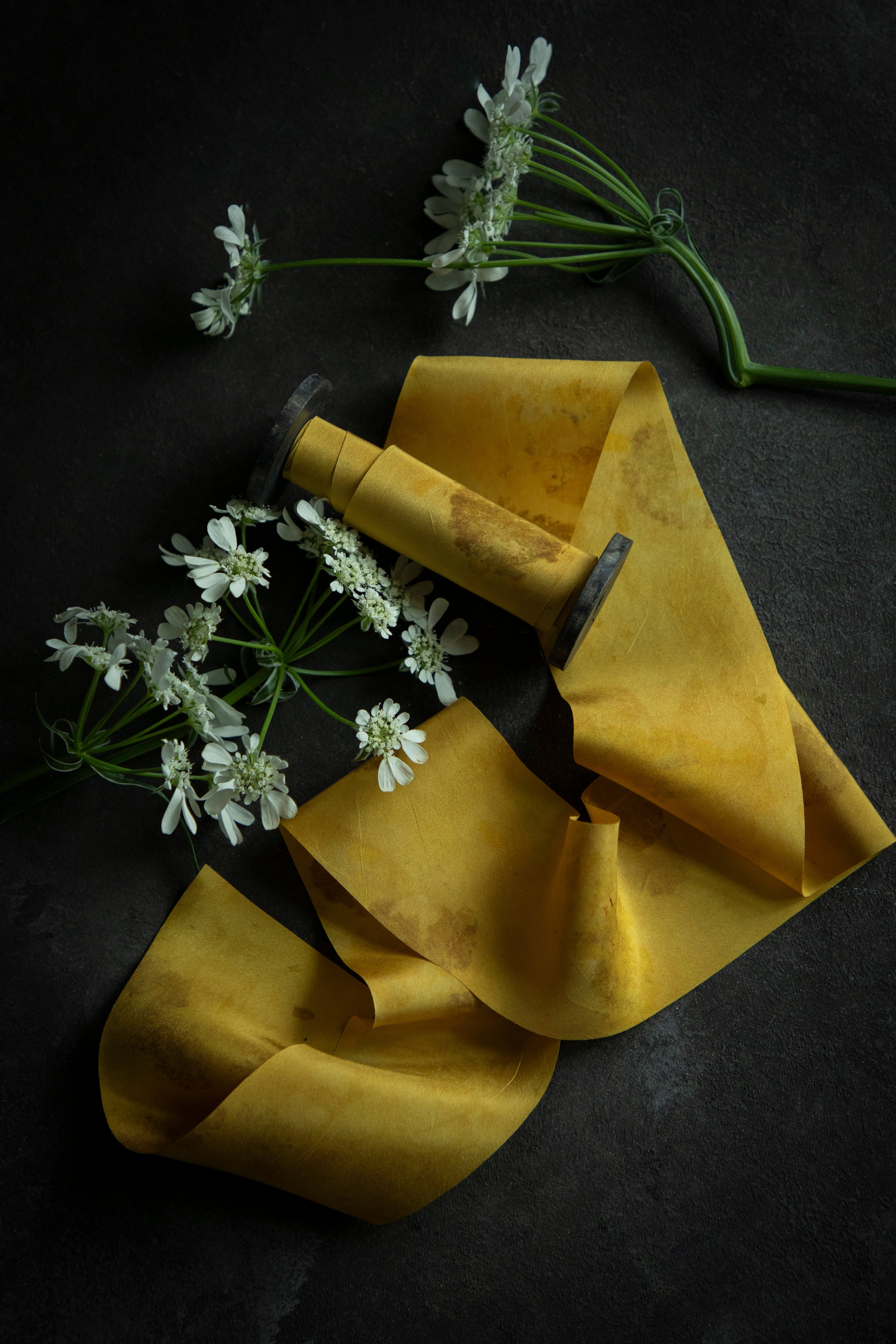 A luminous yellow silk ribbon with a floral pattern, displayed alongside fresh marigold flowers against a dark background.