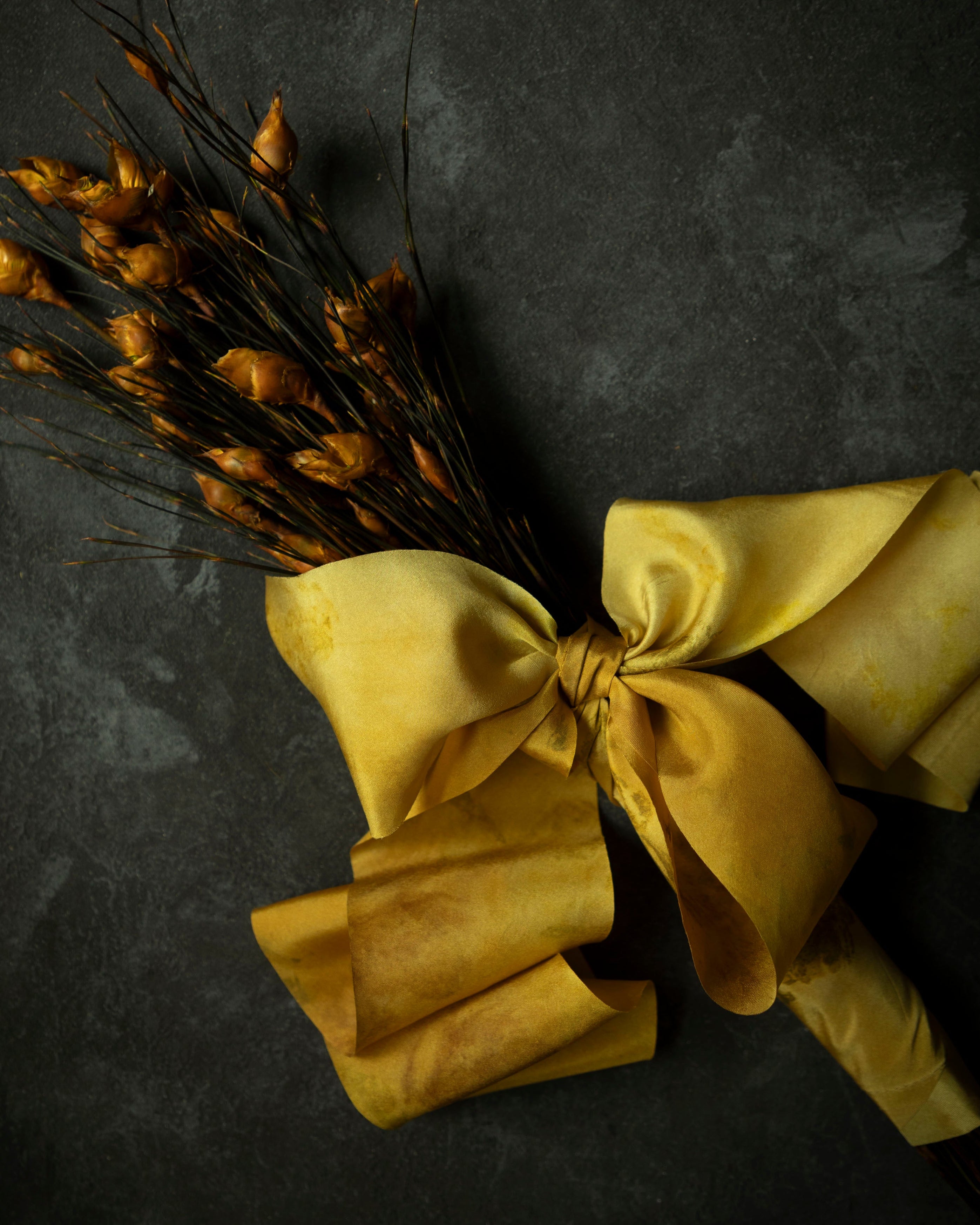 Bouquet of dried yellow flowers with a large yellow bow on a dark background