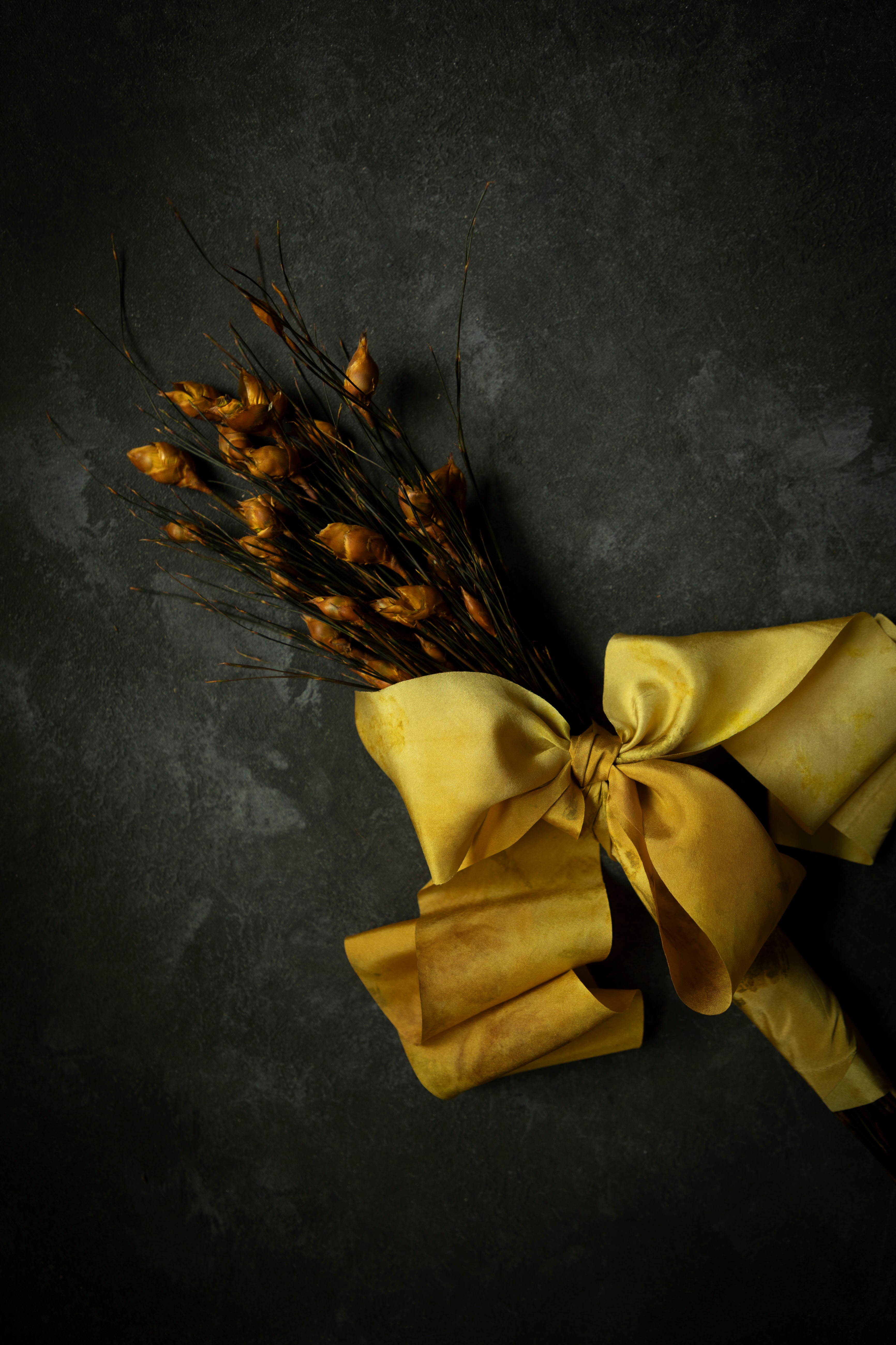 Bouquet of dried yellow flowers with a large yellow bow on a dark background