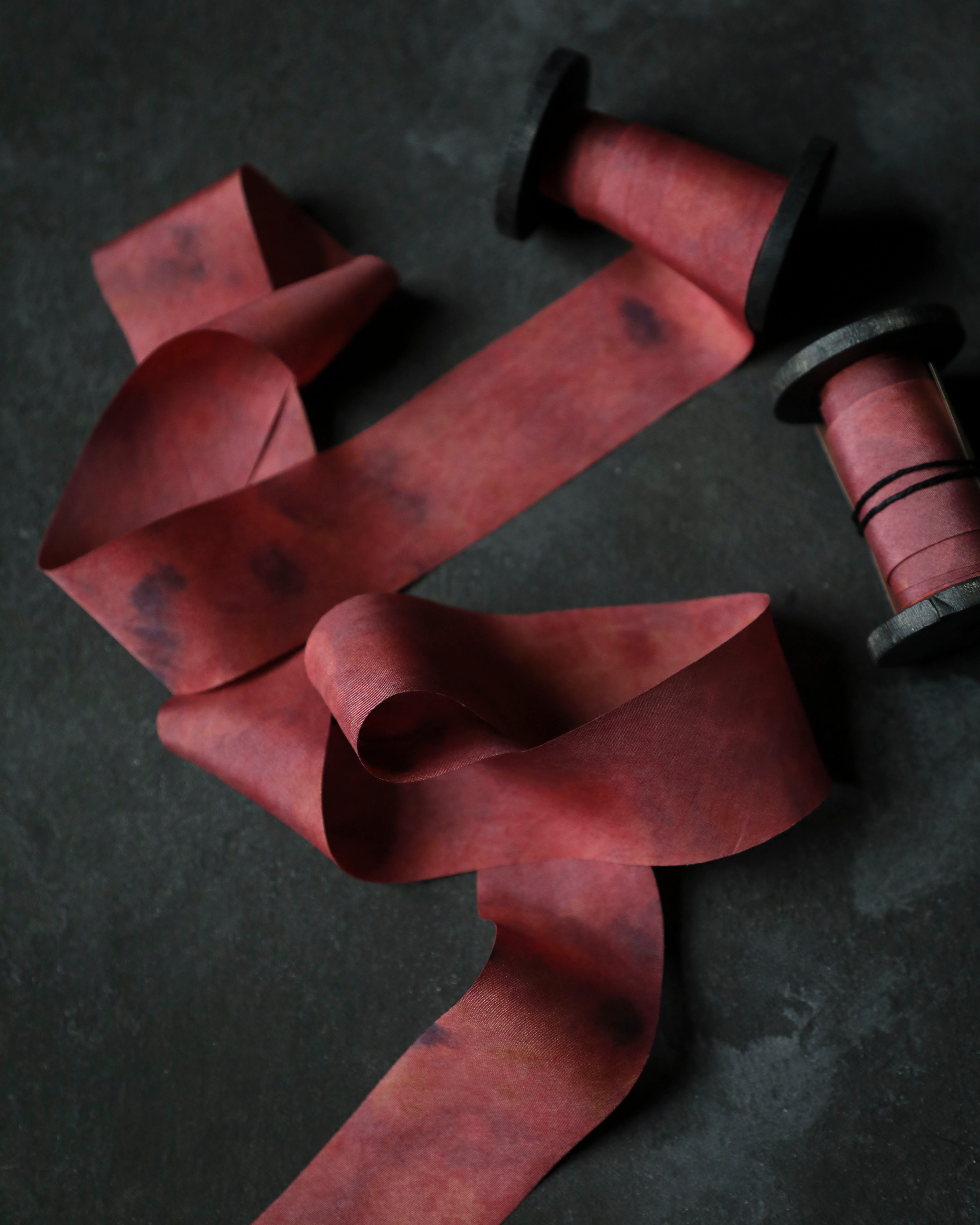 Red ribbon on a dark surface with a spool of thread.