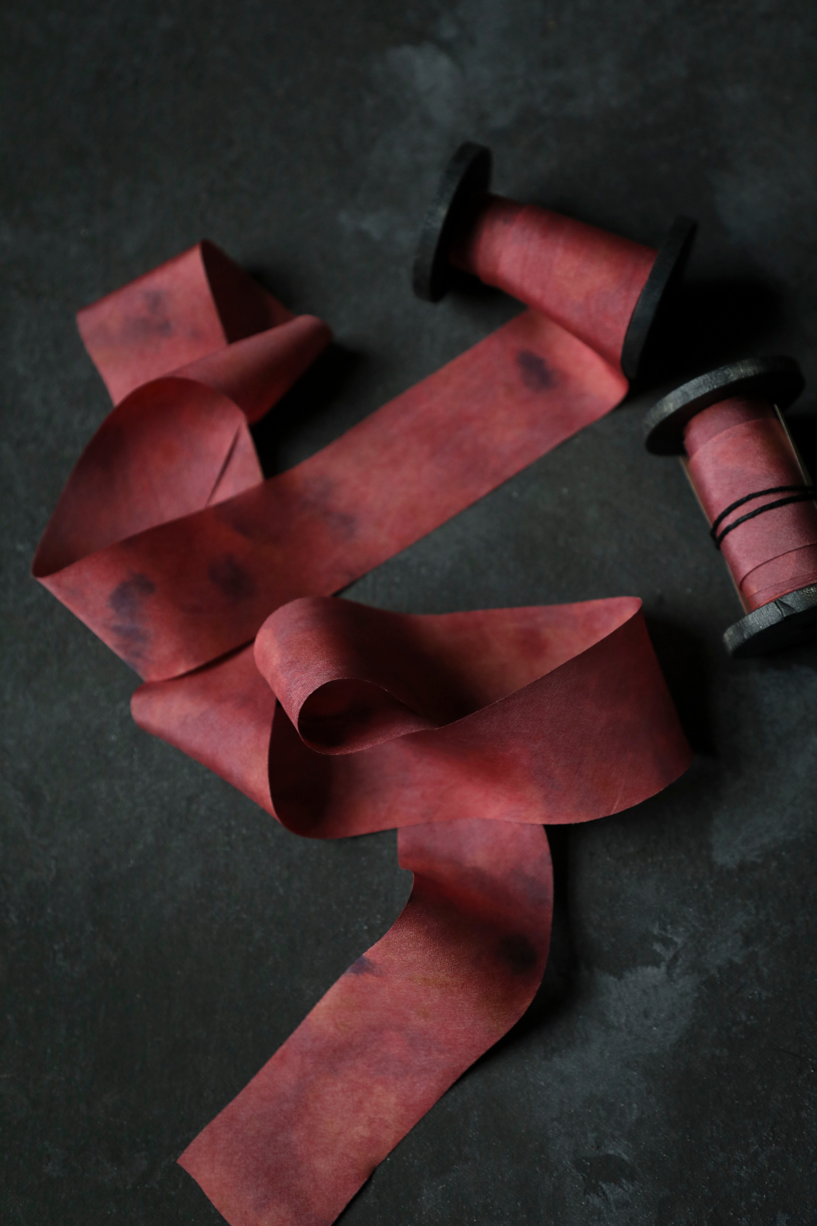Red ribbon on a dark surface with a spool of thread.