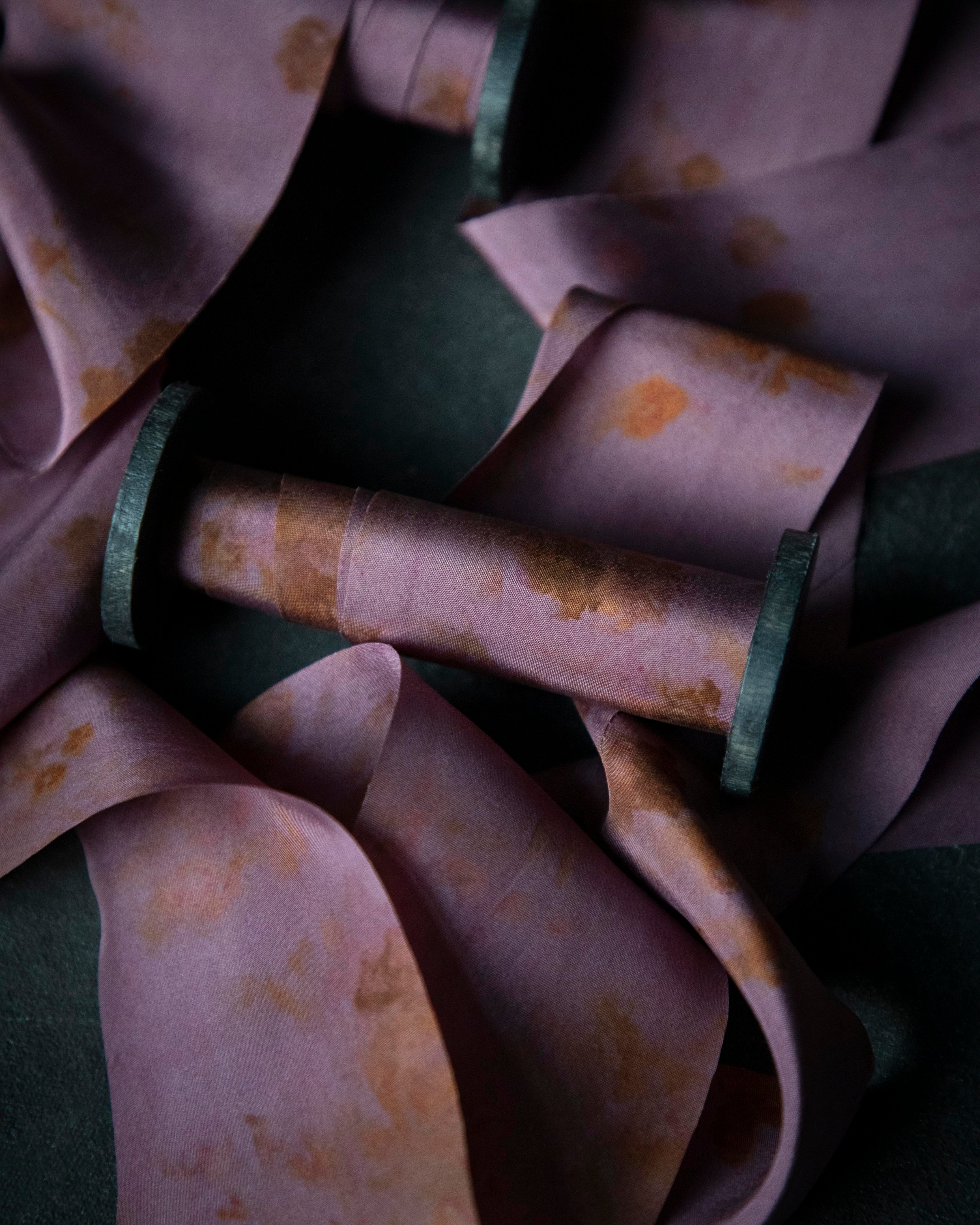 Close-up of a purple fabric with rust-colored stains on a dark background