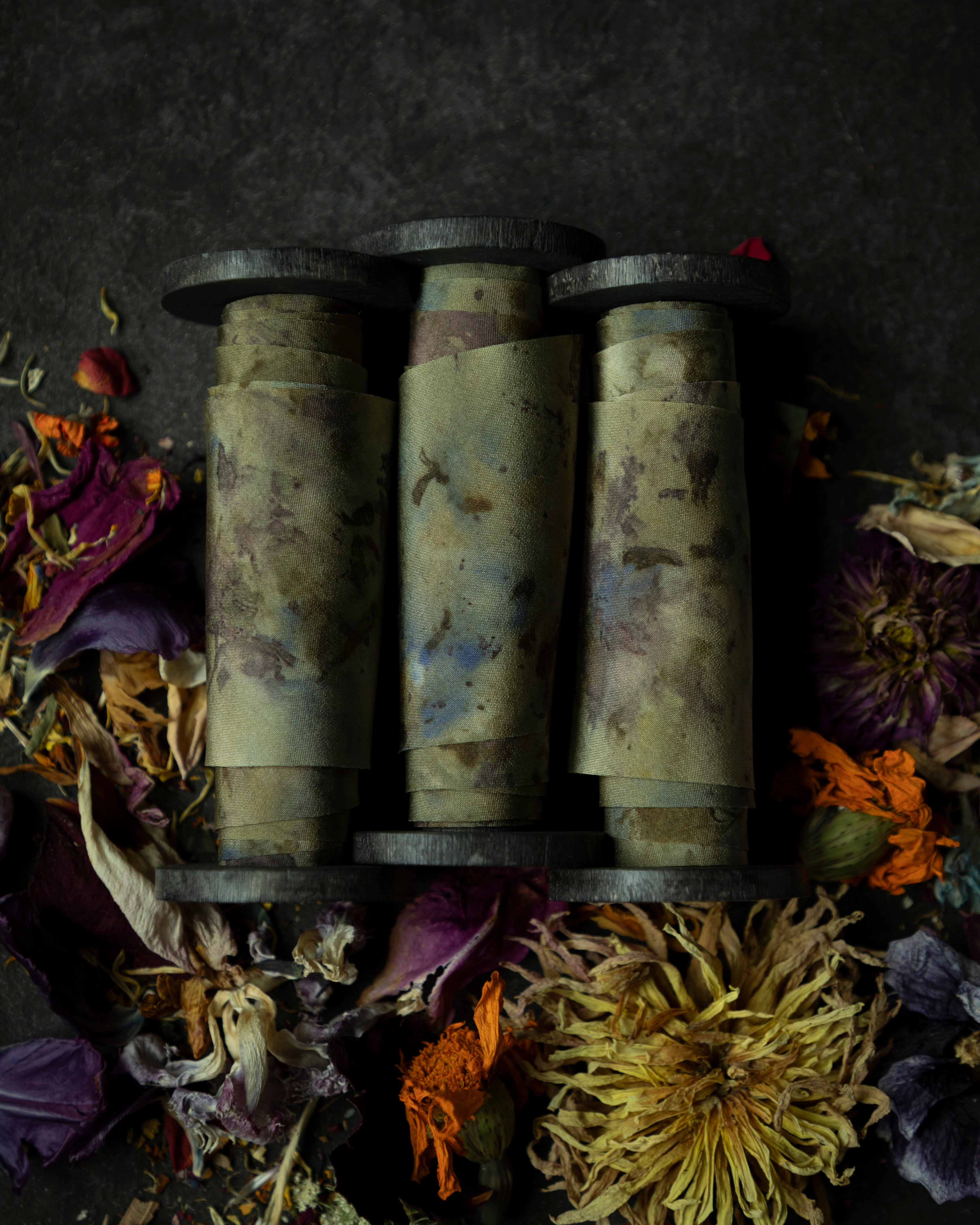 Limited-edition eco-print silk ribbon displayed on a wood spool surrounded by an assortment of dried flowers