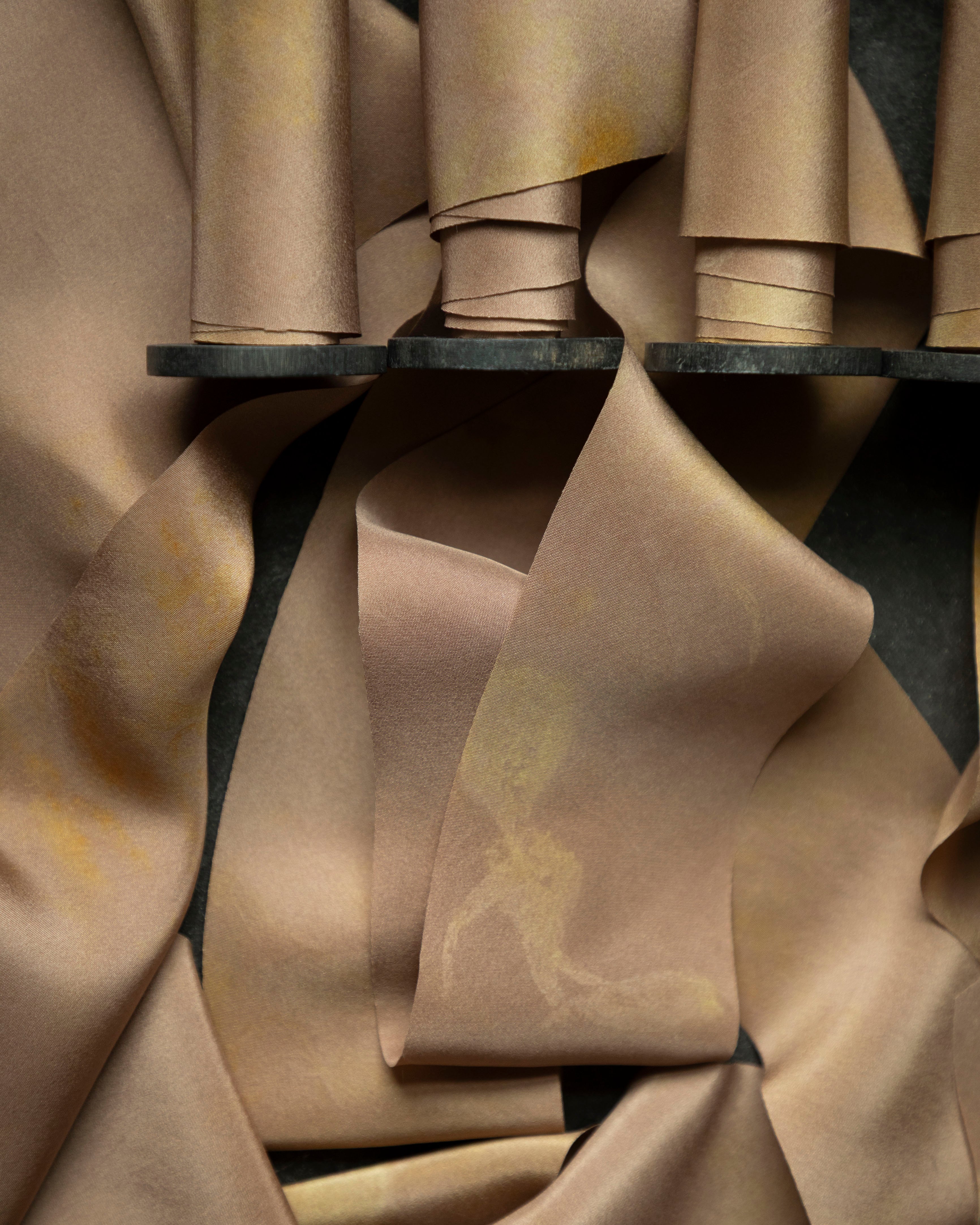 Close-up of silk ribbons on vintage wood spools with folds on a dark background