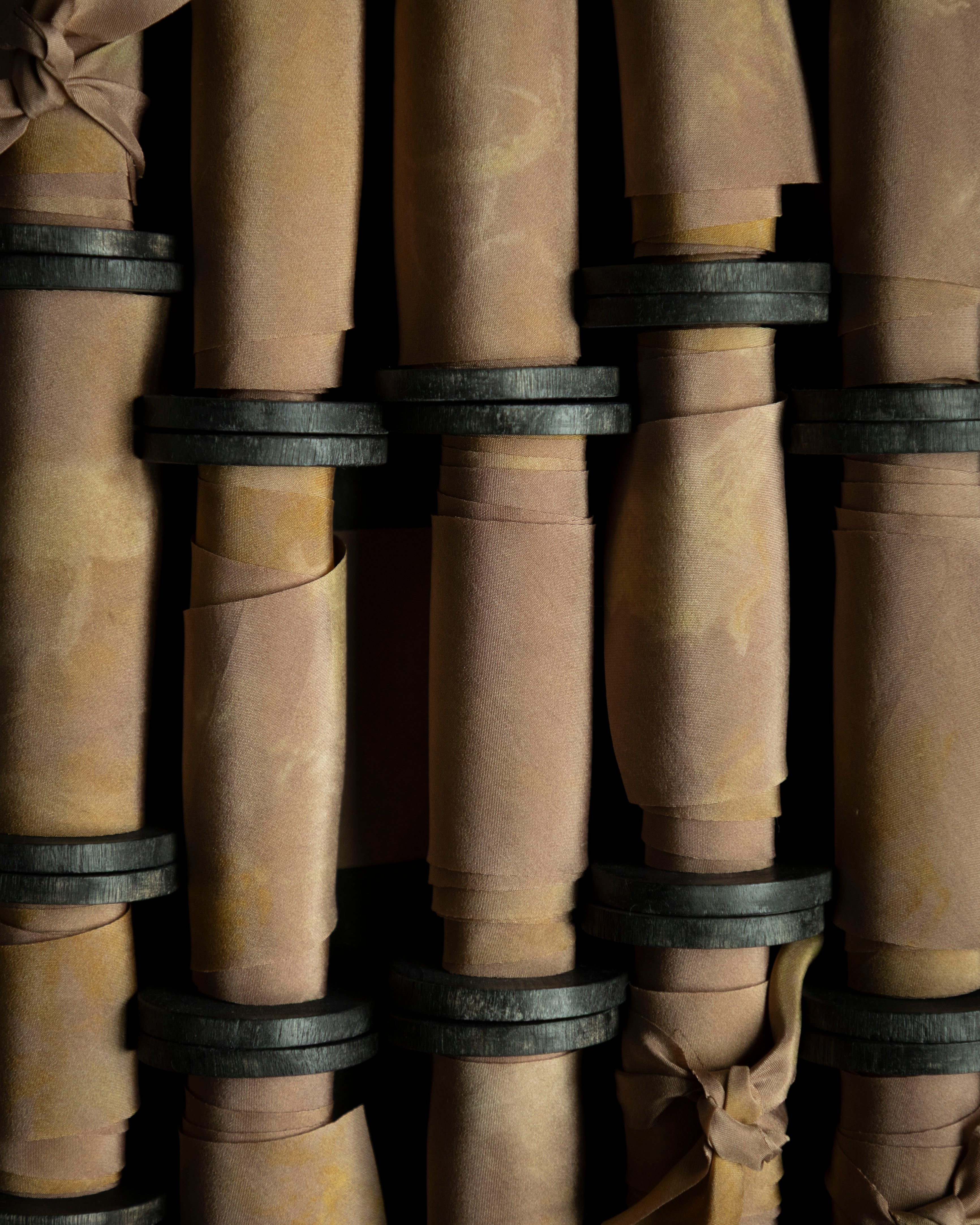 Close-up of hand-dyed silk ribbon on antique wood spools on a dark background