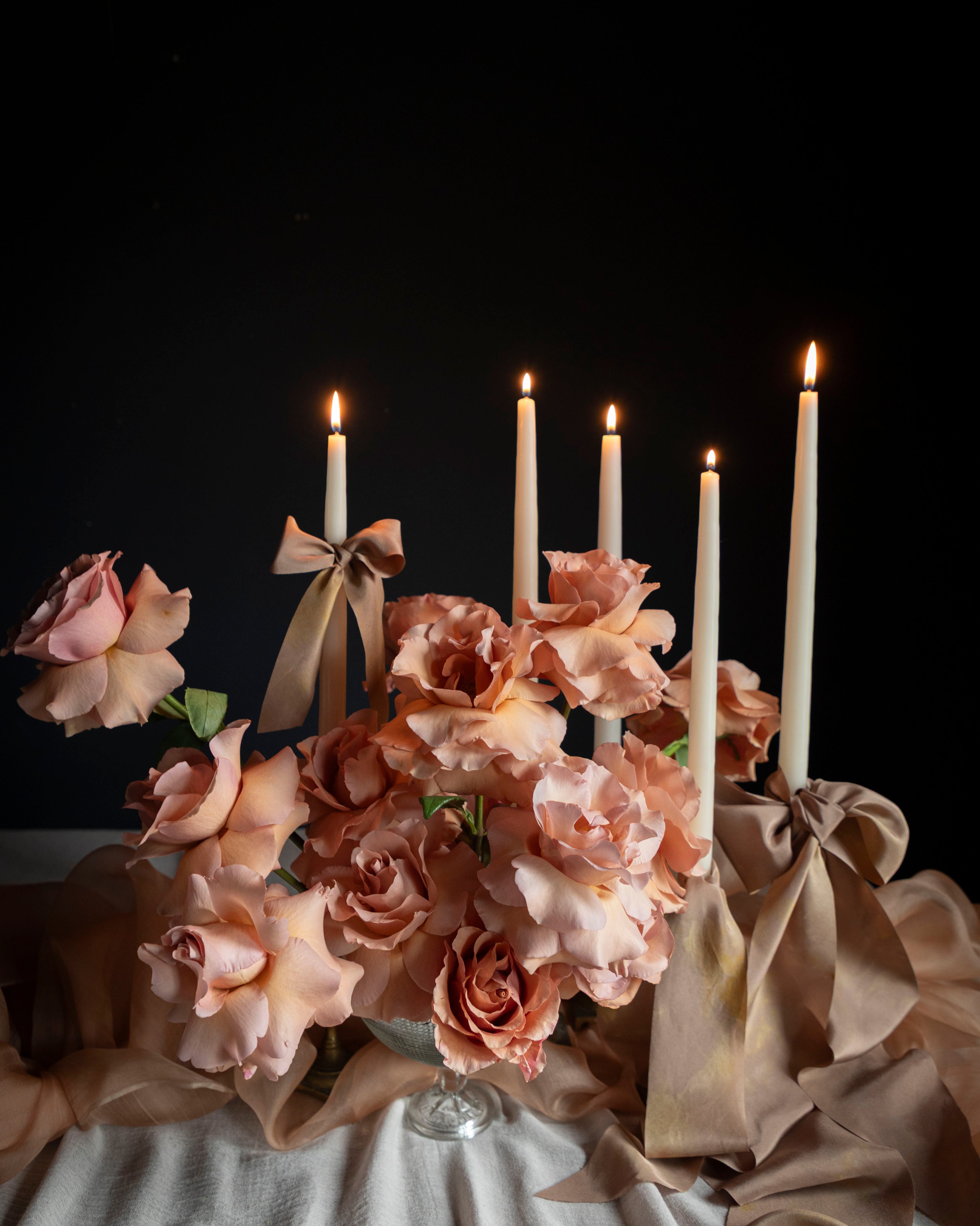 Decorative setup with flowers, candles, and ribbons on a dark background