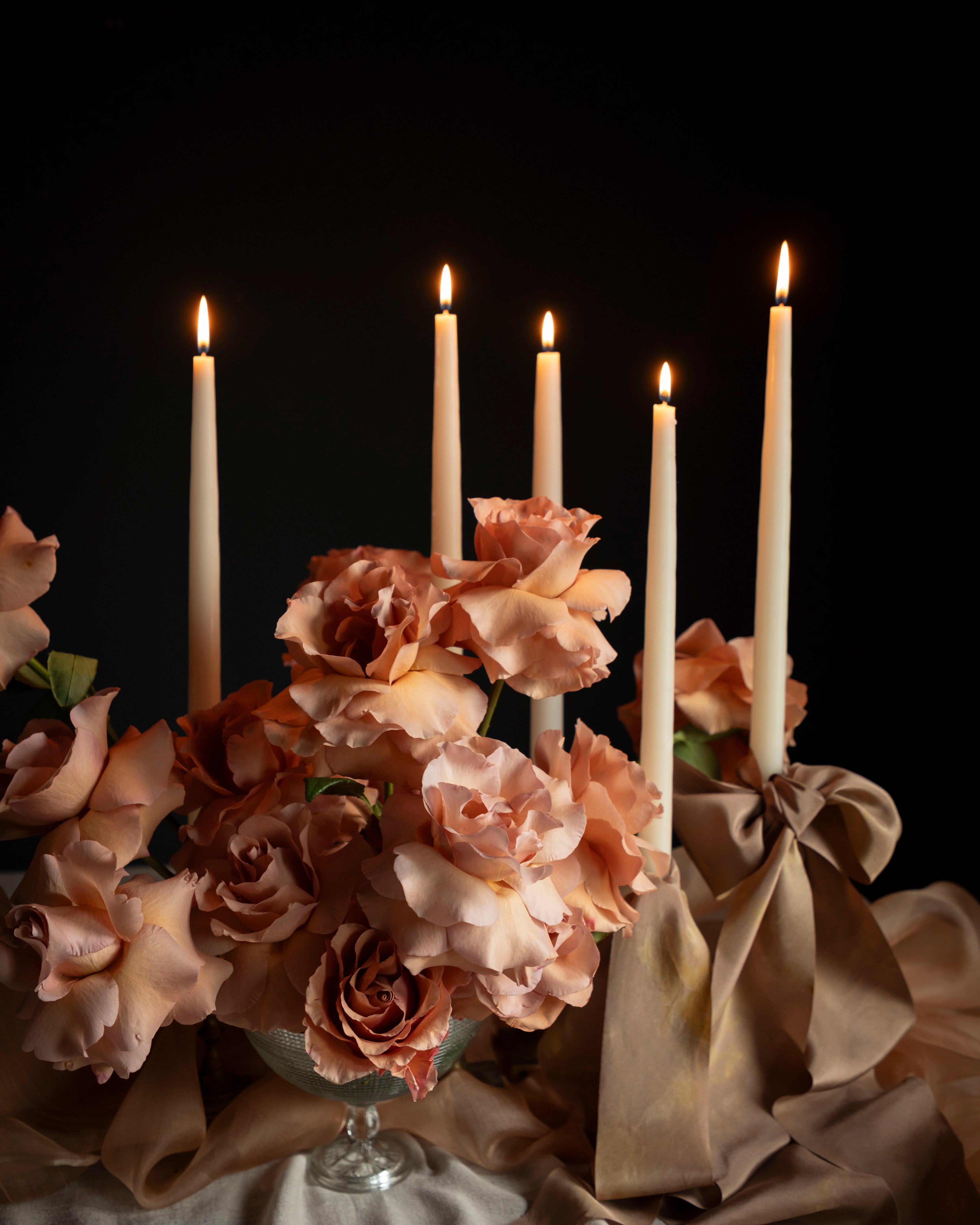 Candlelit scene with flowers and draped fabric against a dark background