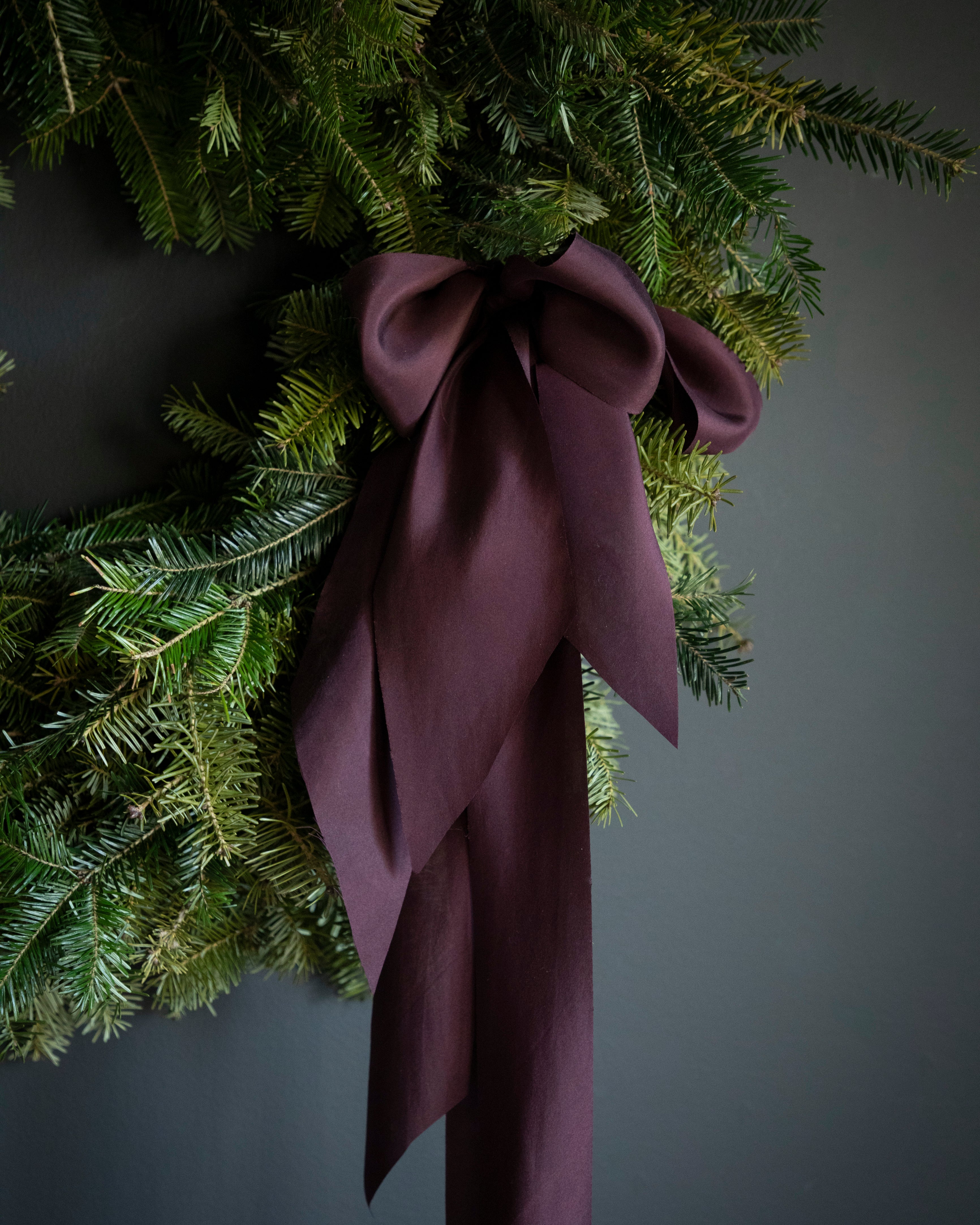 handmade holiday wreath made of evergreens. moody elegance with prple silk ribbons